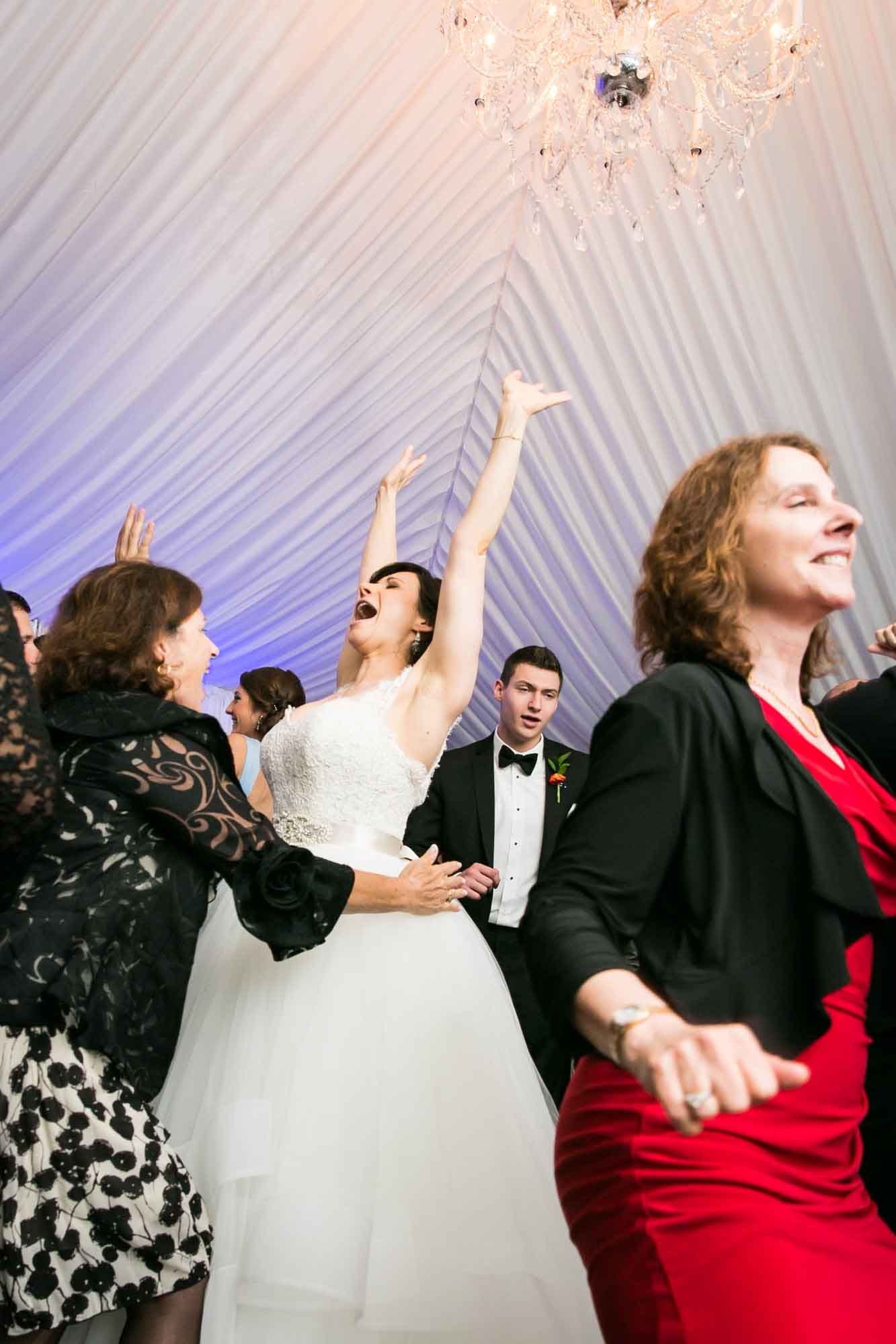 Bride dancing with hands in the air at a Pelham Bay & Split Rock Golf Club wedding reception for an article on what to have ready when the wedding photographer arrives