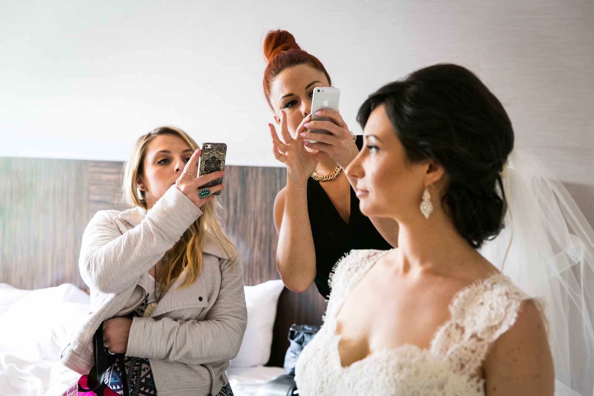 Two women taking cell phone photos of bride before her Fordham University Church wedding for an article on what to have ready when the wedding photographer arrives
