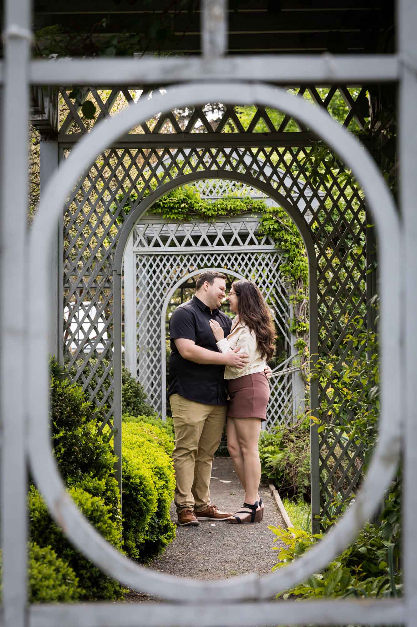 View of couple hugging through lattice garden architecture for article on best Ziliker Botanical Garden photo locations