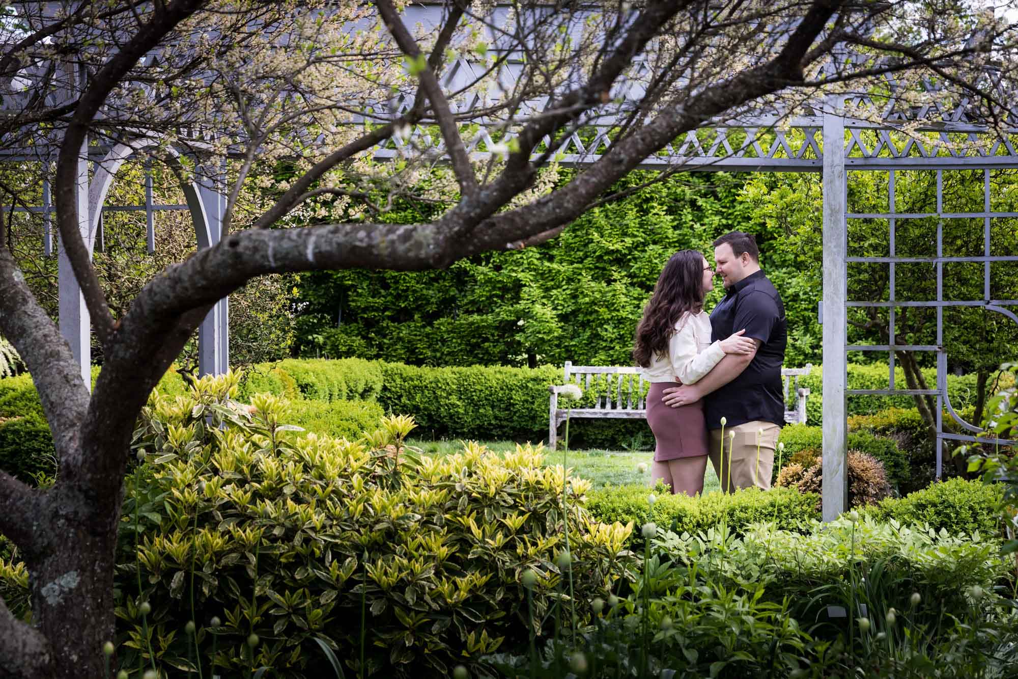 Couple hugging in front of bench and green bushes for article on best Ziliker Botanical Garden photo locations