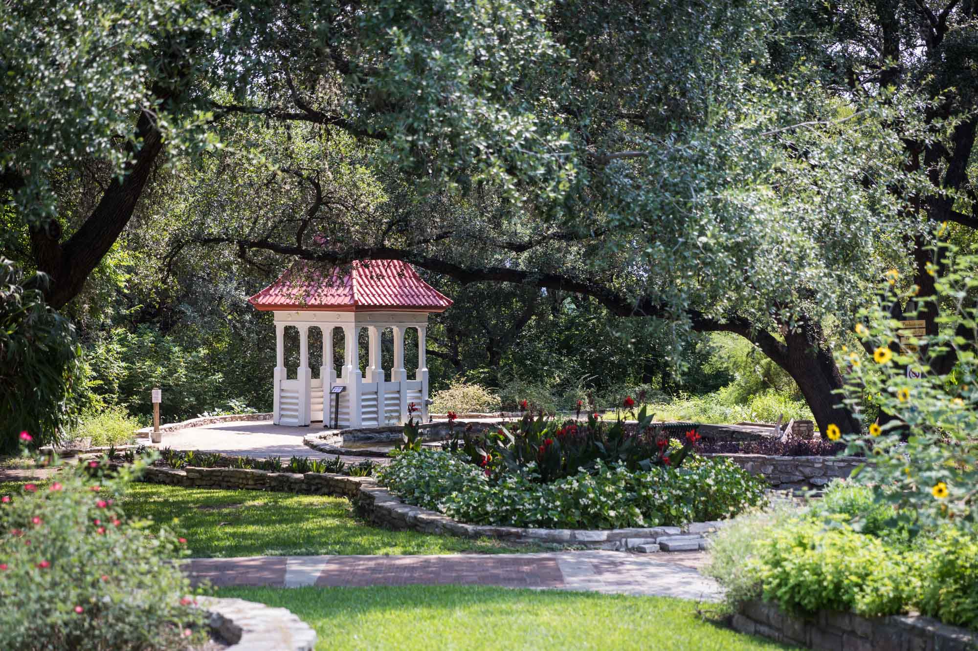 White gazebo with red roof surrounded by trees for an article on the best Zilker Botanical Garden photo locations
