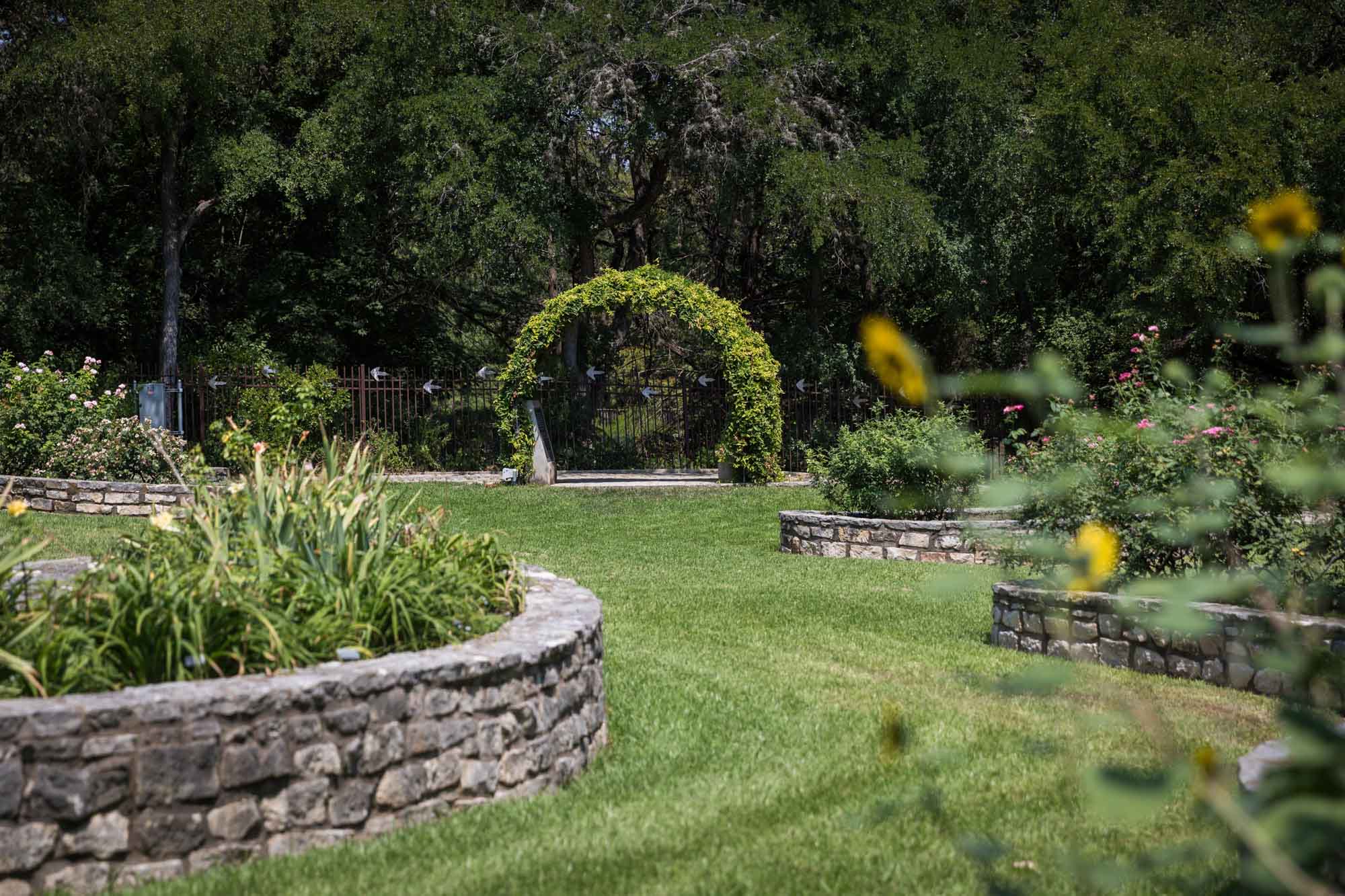 Stone walled garden beds and green lawn with vine-covered arch for an article on the best Zilker Botanical Garden photo locations