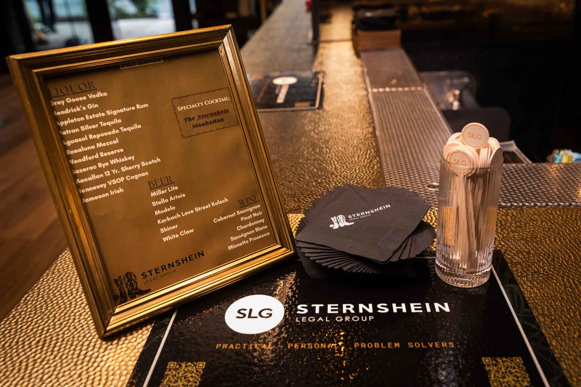 Frame showing available drinks next to printed cocktail napkins and glass holding cocktail stirrers on bar during a Hotel Van Zandt corporate event