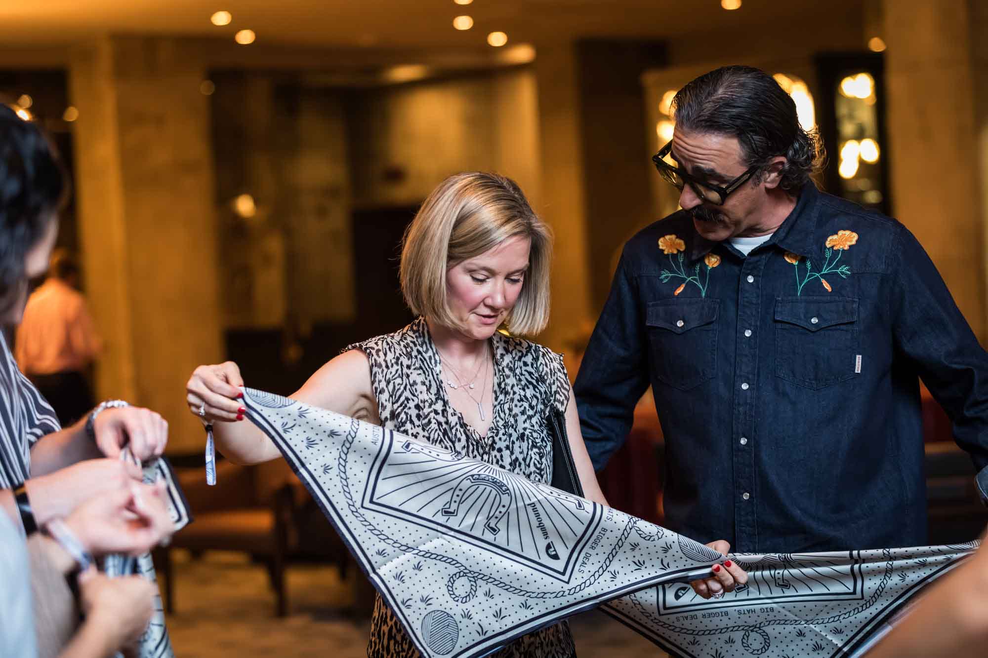 Woman holding a silk scarf outstretched with man wearing denim shirt standing next to her during a Hotel Van Zandt corporate event