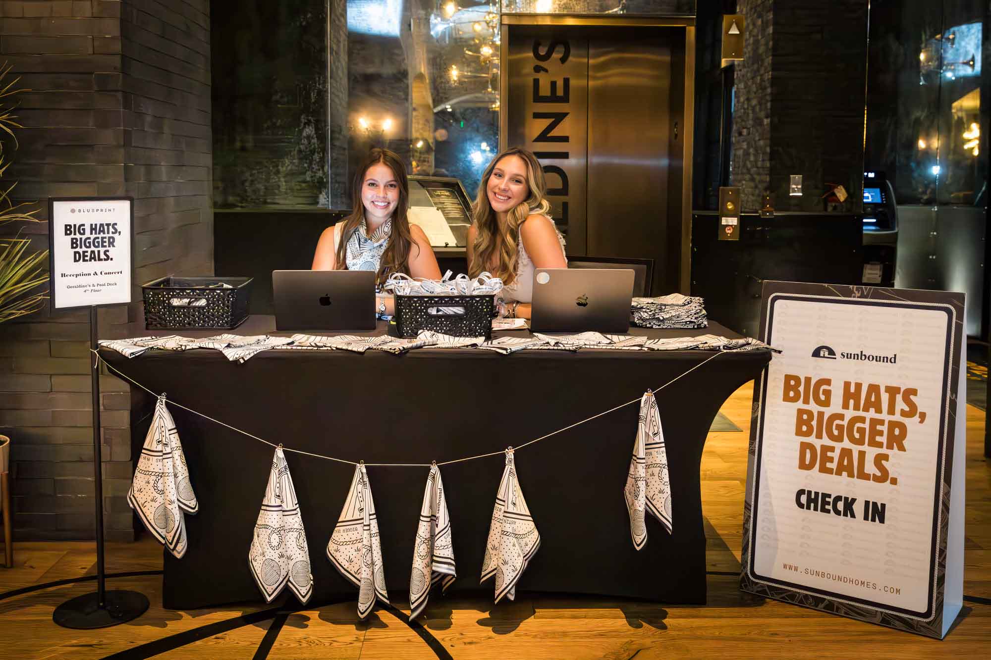 Two women sitting at registration table with sign to the right and string holding silk scarves in the front during a Hotel Van Zandt corporate event