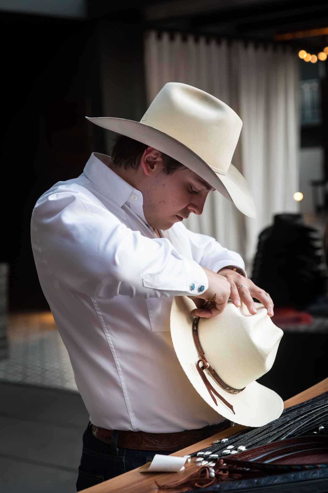 Man wearing white cowboy hat and white shirt putting special belt around white cowboy hat during a Hotel Van Zandt corporate event
