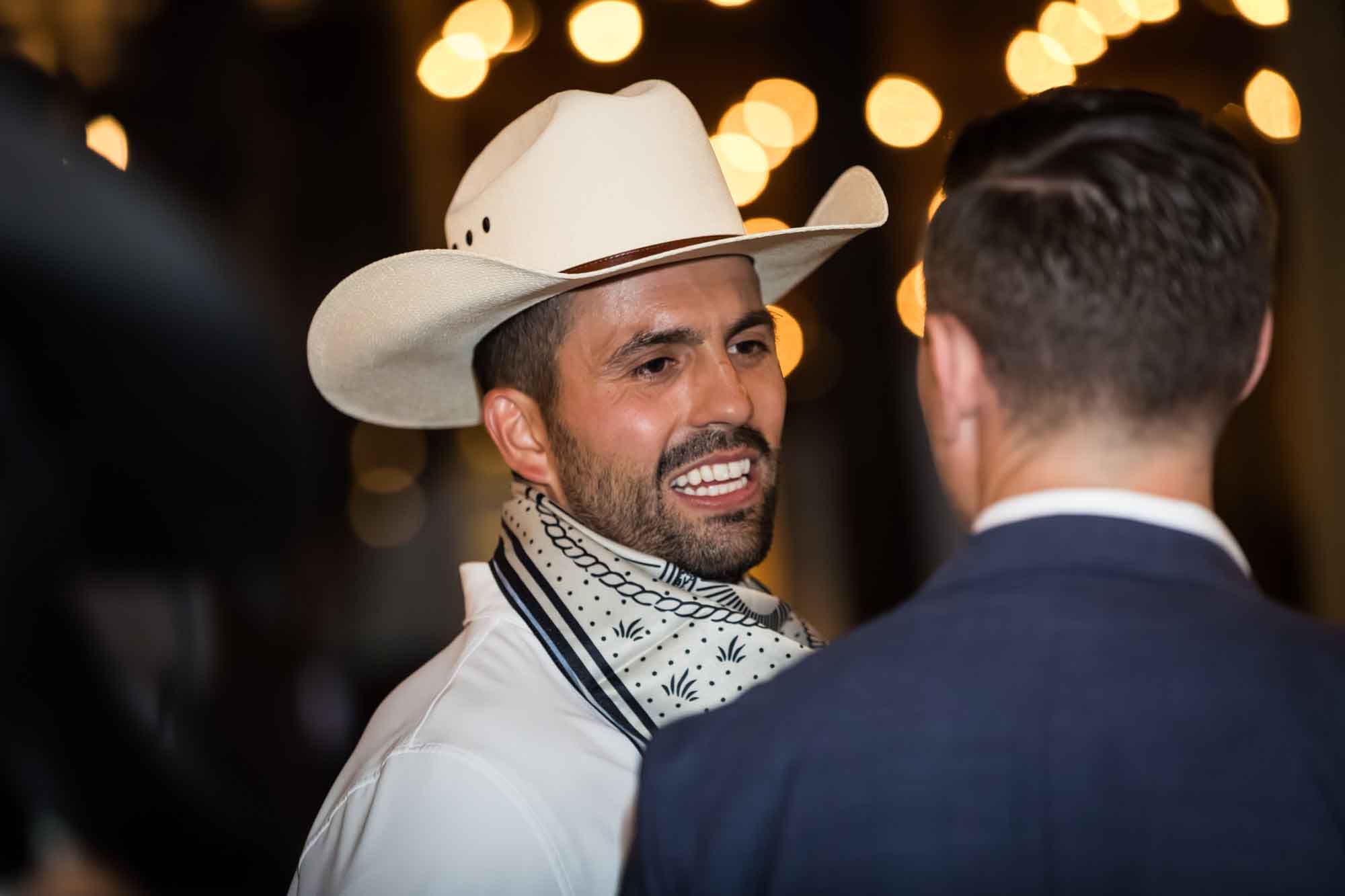 Man wearing white cowboy hat and silk scarf with lights in background talking to another man during a Hotel Van Zandt corporate event