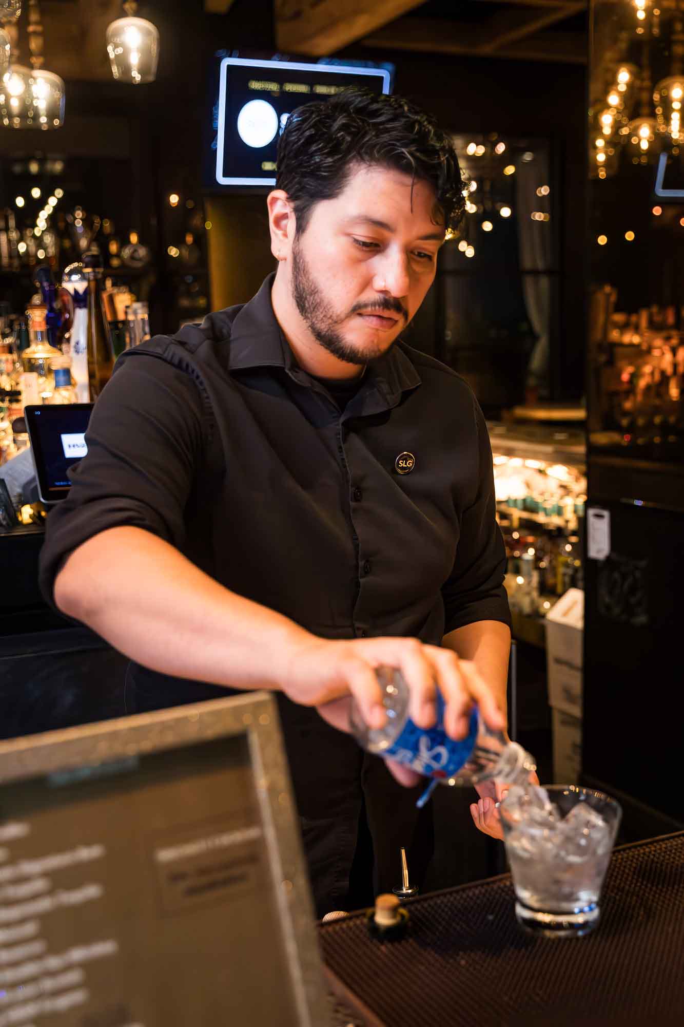 Bartender with black hair pouring contents of bottle into glass at bar during a Hotel Van Zandt corporate event