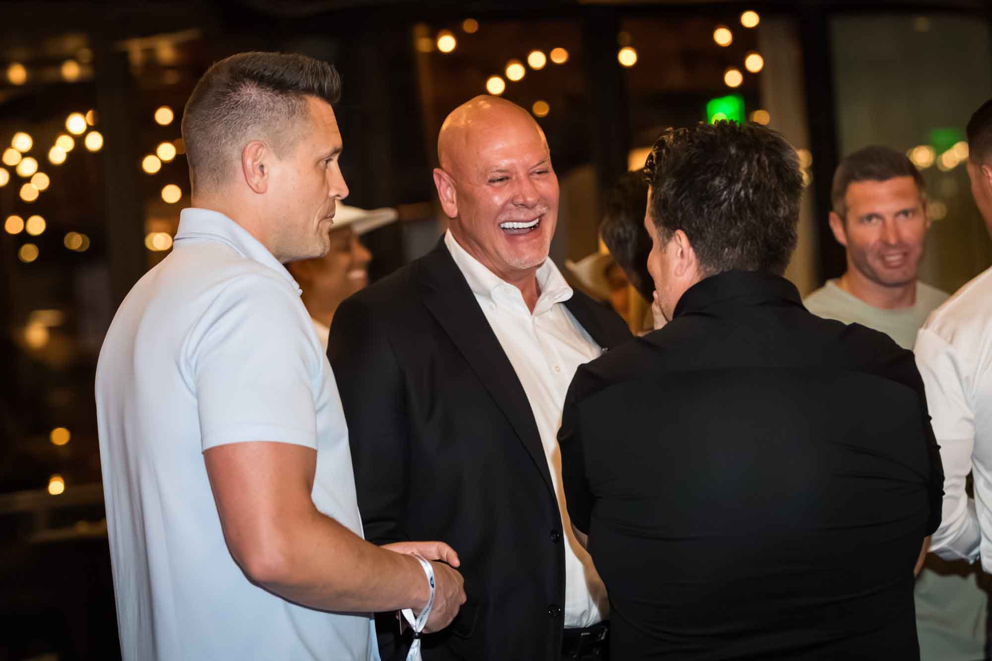 Bald man wearing white shirt and black jacket laughing and talking to two other men during a Hotel Van Zandt corporate event