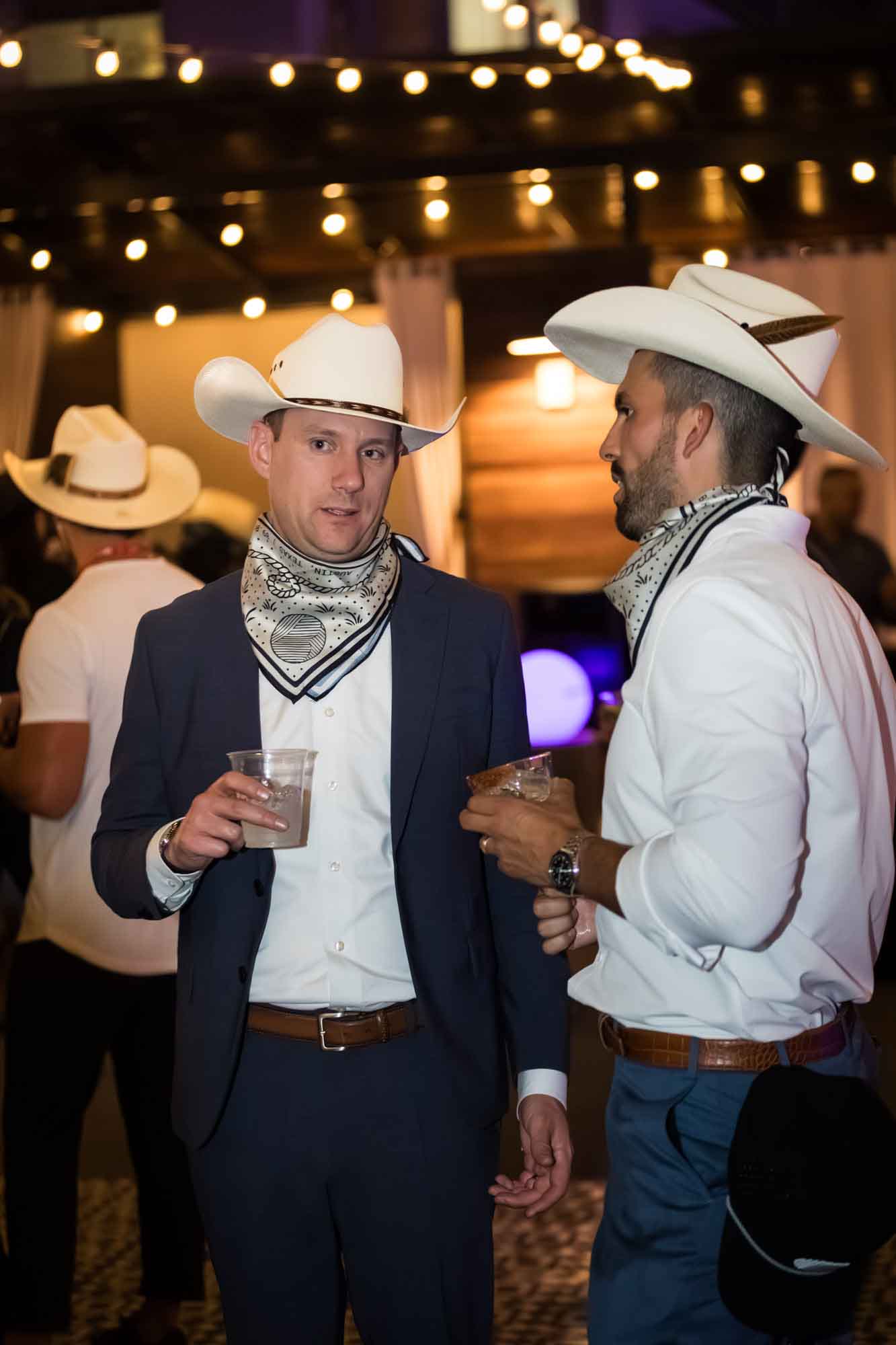 Two men wearing white cowboy hats and silk scarves around their necks during a Hotel Van Zandt corporate event