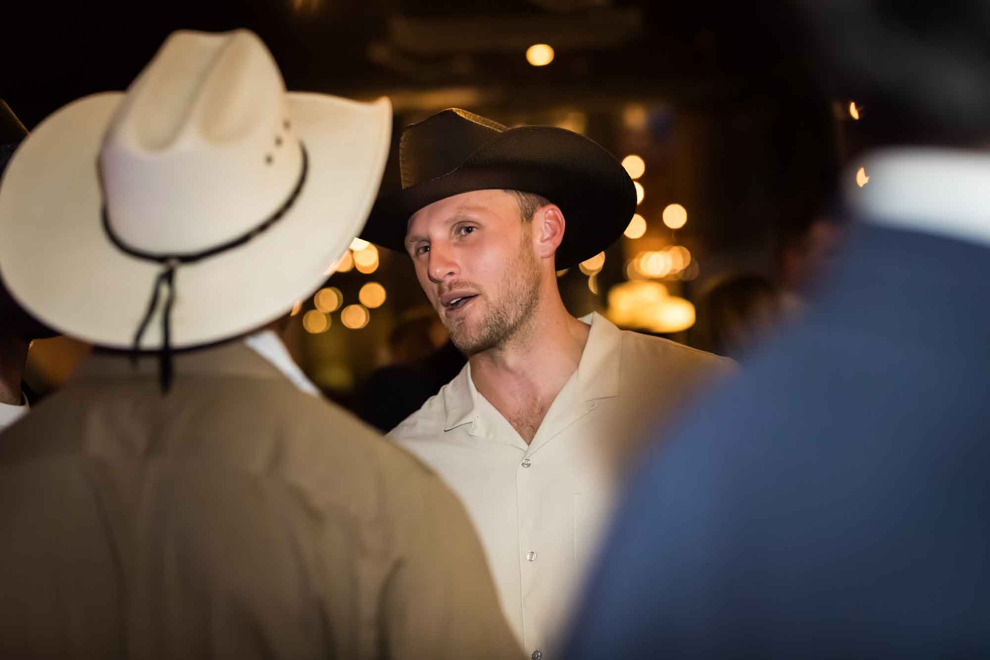 Man wearing beige shirt and brown cowboy hat behind man wearing white cowboy hat during a Hotel Van Zandt corporate event