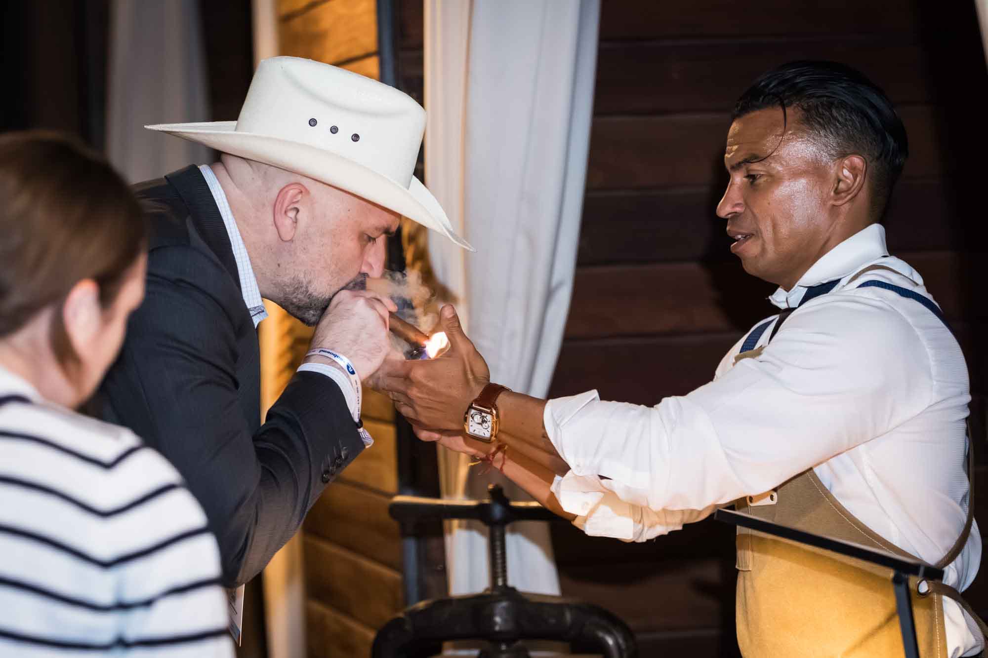 Ibrahim Ruiz lighting a cigar for a man wearing a white cowboy hat during a Hotel Van Zandt corporate event
