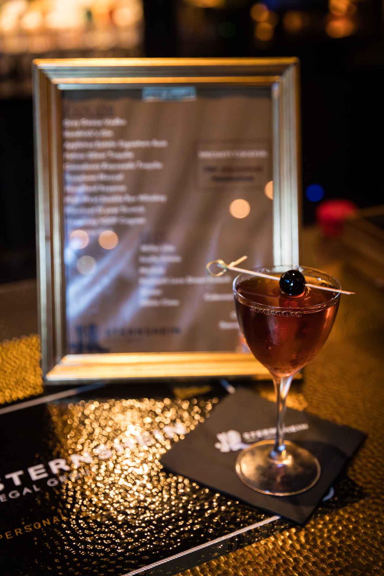 Small glass with Manhattan cocktail drink with cocktail pick and cherry on top and frame behind drink on bar during a Hotel Van Zandt corporate event