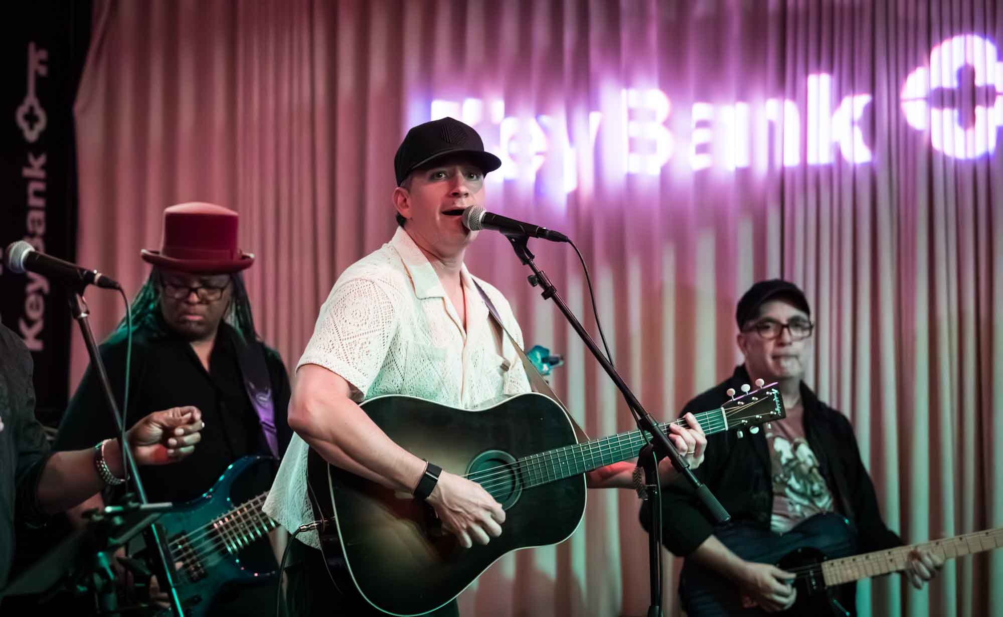 Goldford musician playing black guitar in front of two guitarists and curtain during a Hotel Van Zandt corporate event