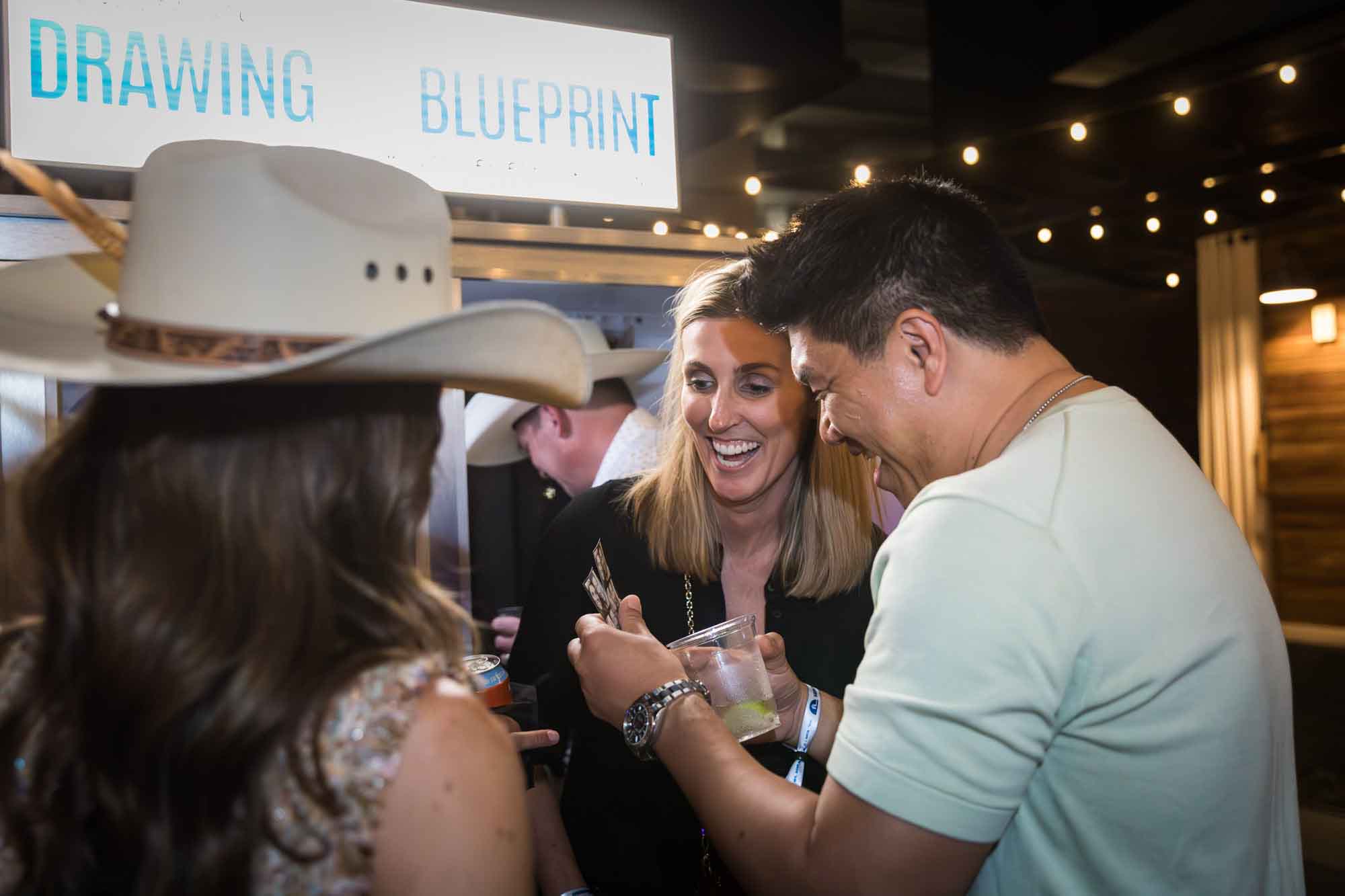 Asian man and blonde-haired woman smiling while looking at strip of photo booth photos in front of photo booth during a Hotel Van Zandt corporate event