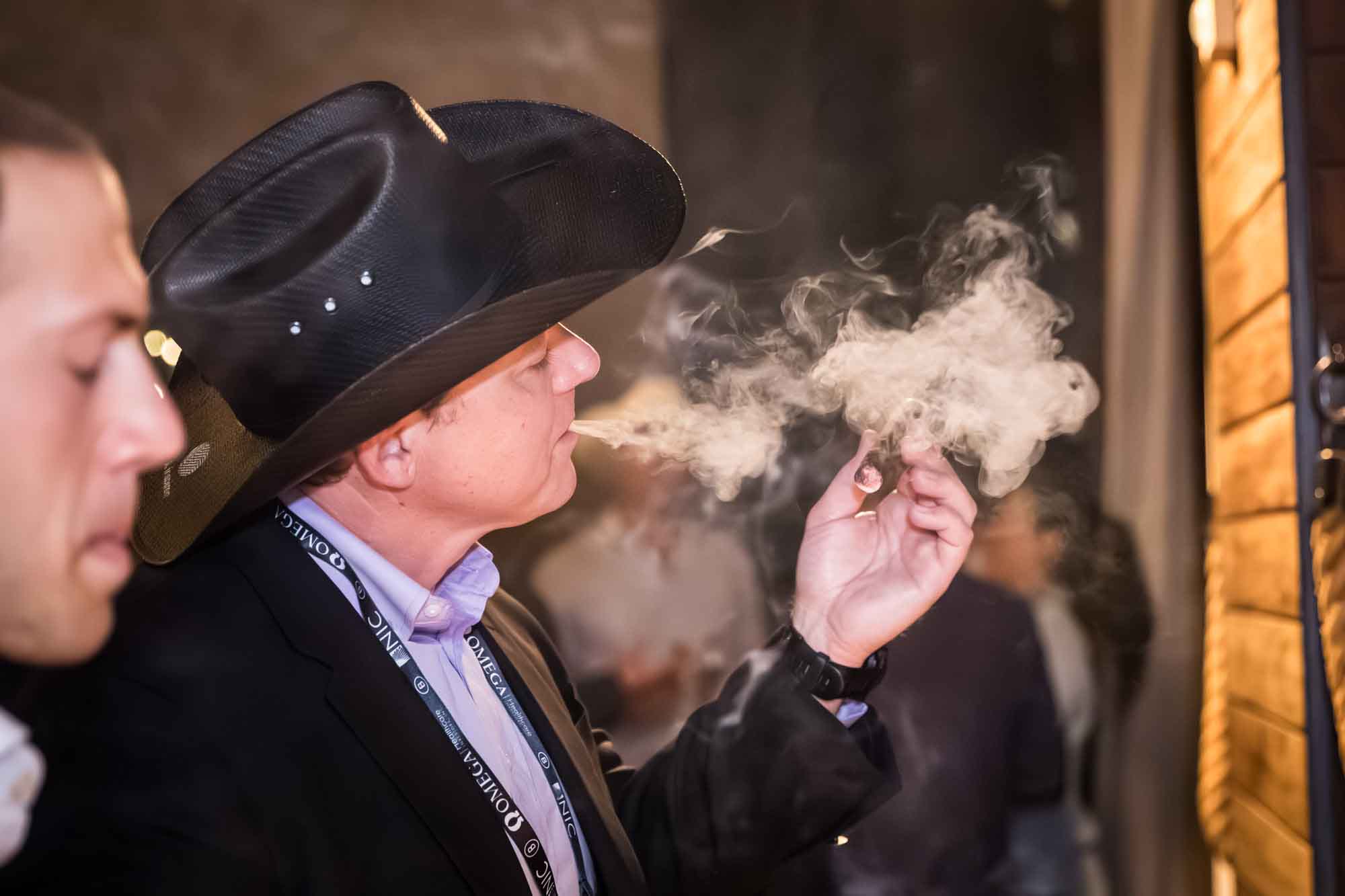 Man wearing black cowboy hat blowing smoke while holding cigar during a Hotel Van Zandt corporate event