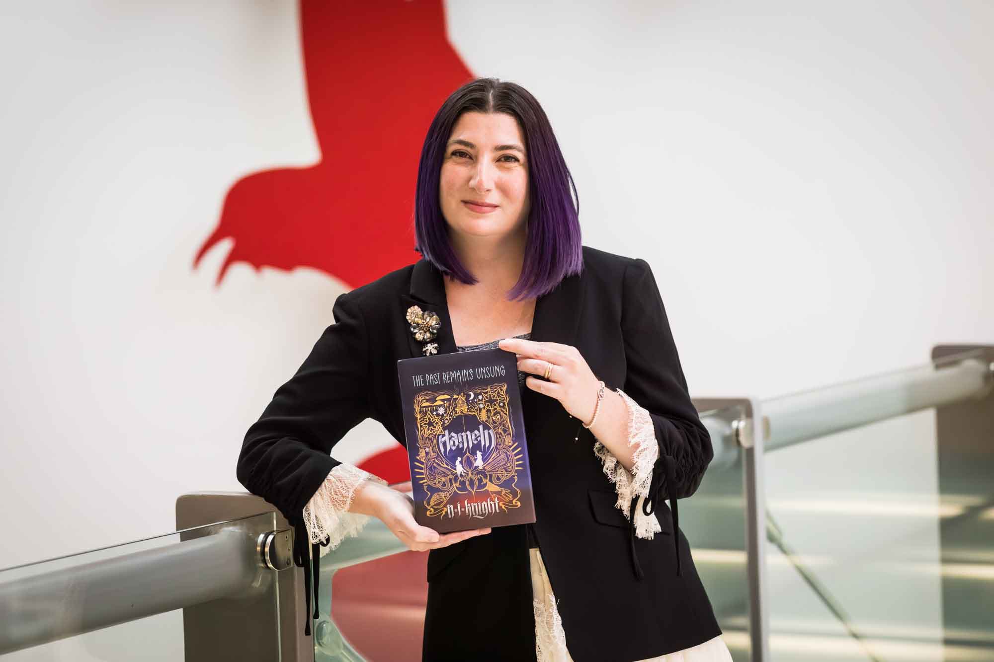 Author Nancy Knight holding her book Hameln in front of a red art installation for an article on how to take photos in the Austin Central Library