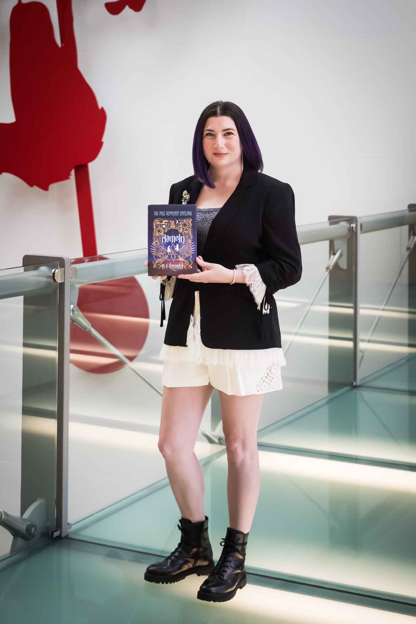 Author Nancy Knight holding her book Hameln in front of a red art installation for an article on how to take photos in the Austin Central Library