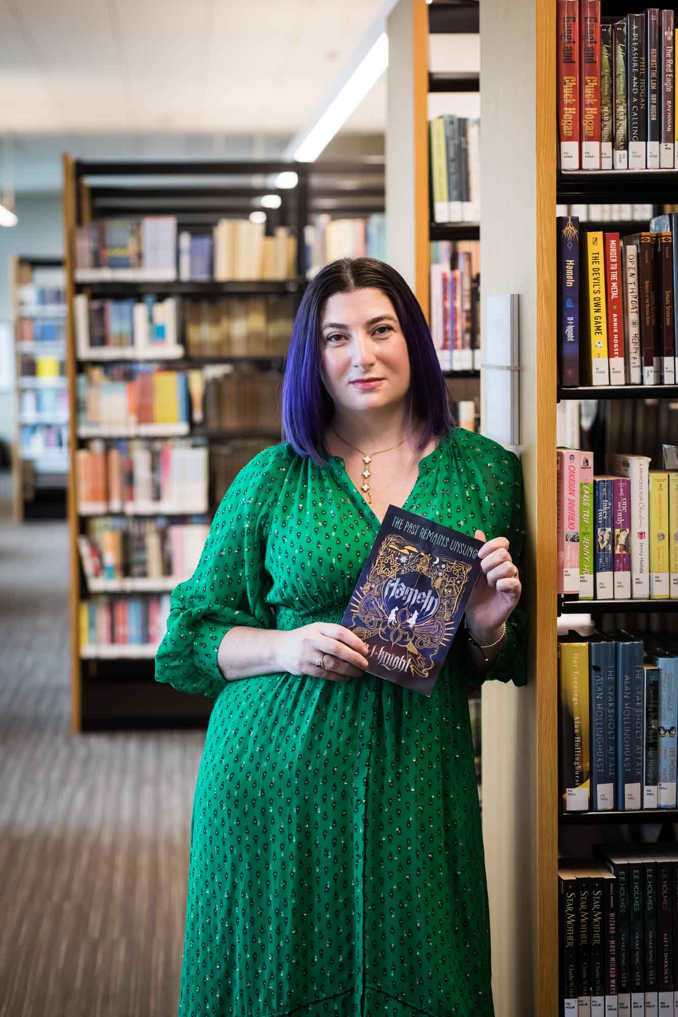 Portrait of author Nancy Knight in the Austin Central Library wearing a green dress holding her book, Hameln