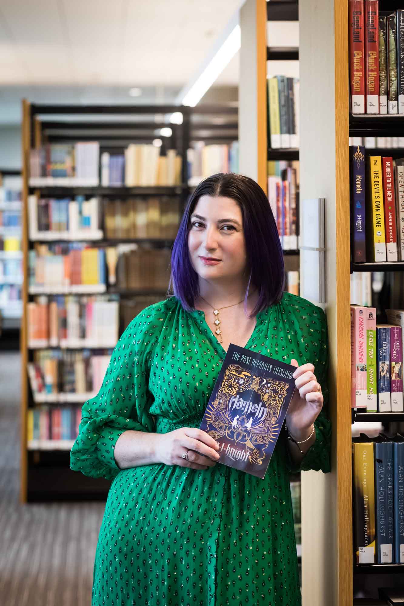 Portrait of author Nancy Knight in the Austin Central Library wearing a green dress holding her book, Hameln