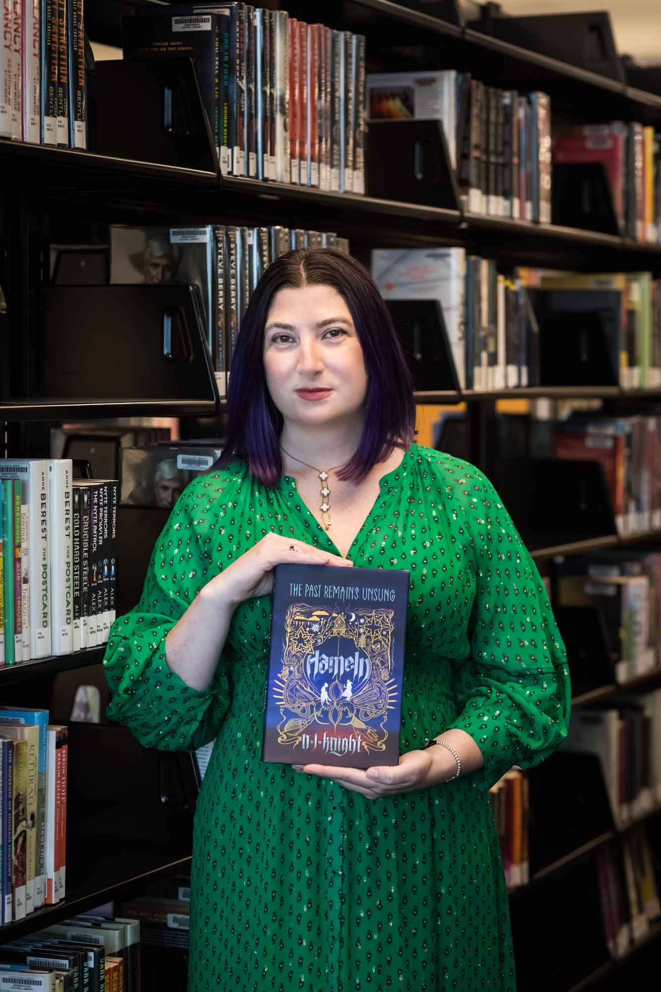 Portrait of author Nancy Knight in the Austin Central Library wearing a green dress holding her book, Hameln