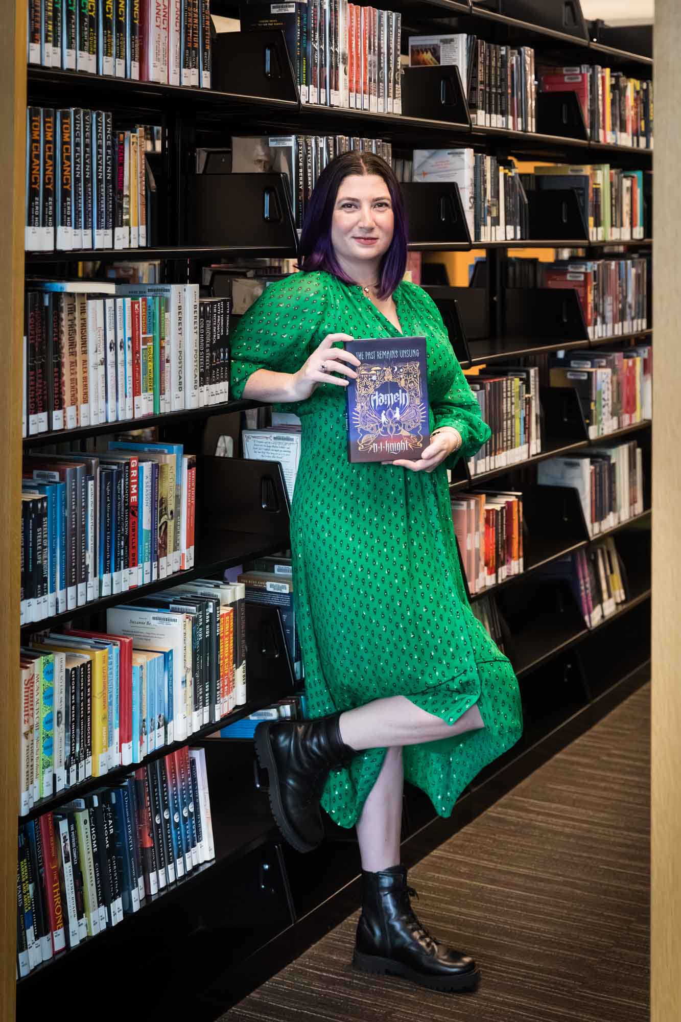 Portrait of author Nancy Knight in the Austin Central Library wearing a green dress holding her book, Hameln