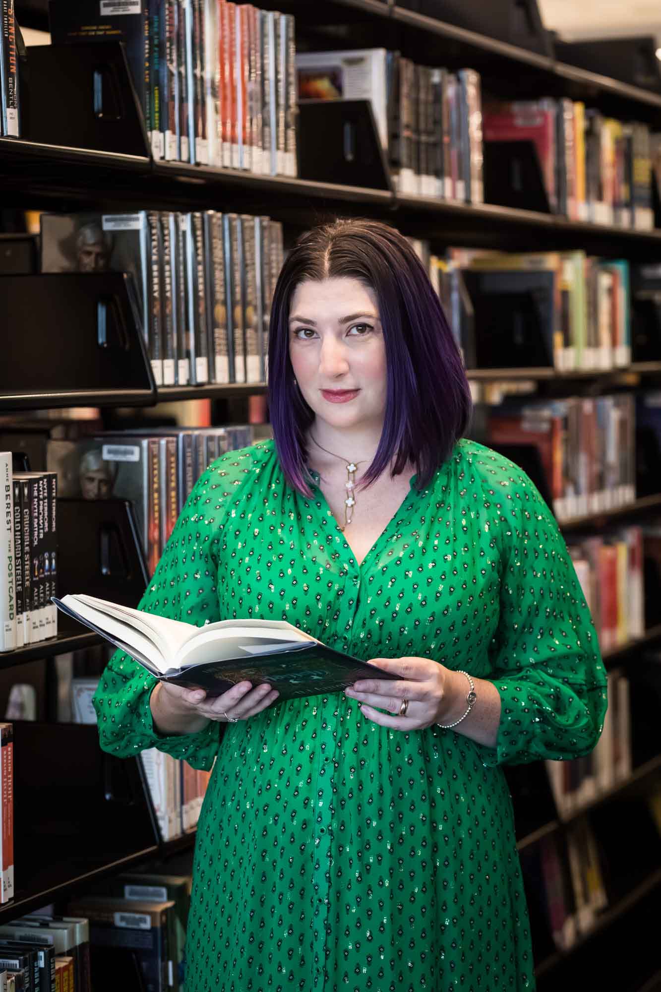 Author Nancy Knight wearing a green dress and reading her book Hameln for an article on how to take photos in the Austin Central Library