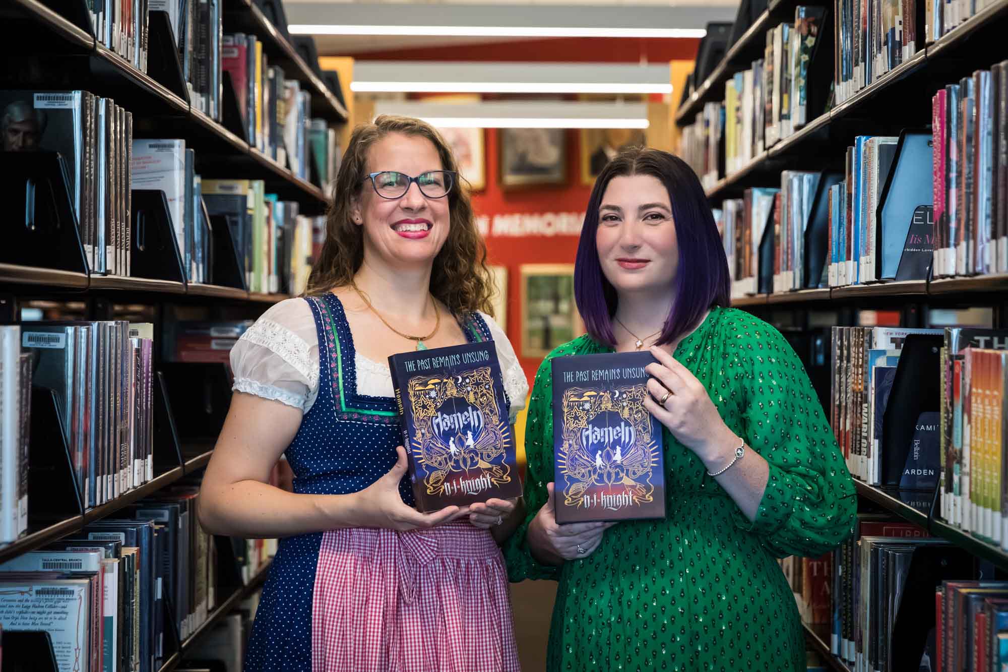 Author Nancy Knight and editor Britta Jensen holding books in front of bookshelves for an article on how to take photos in the Austin Central Library