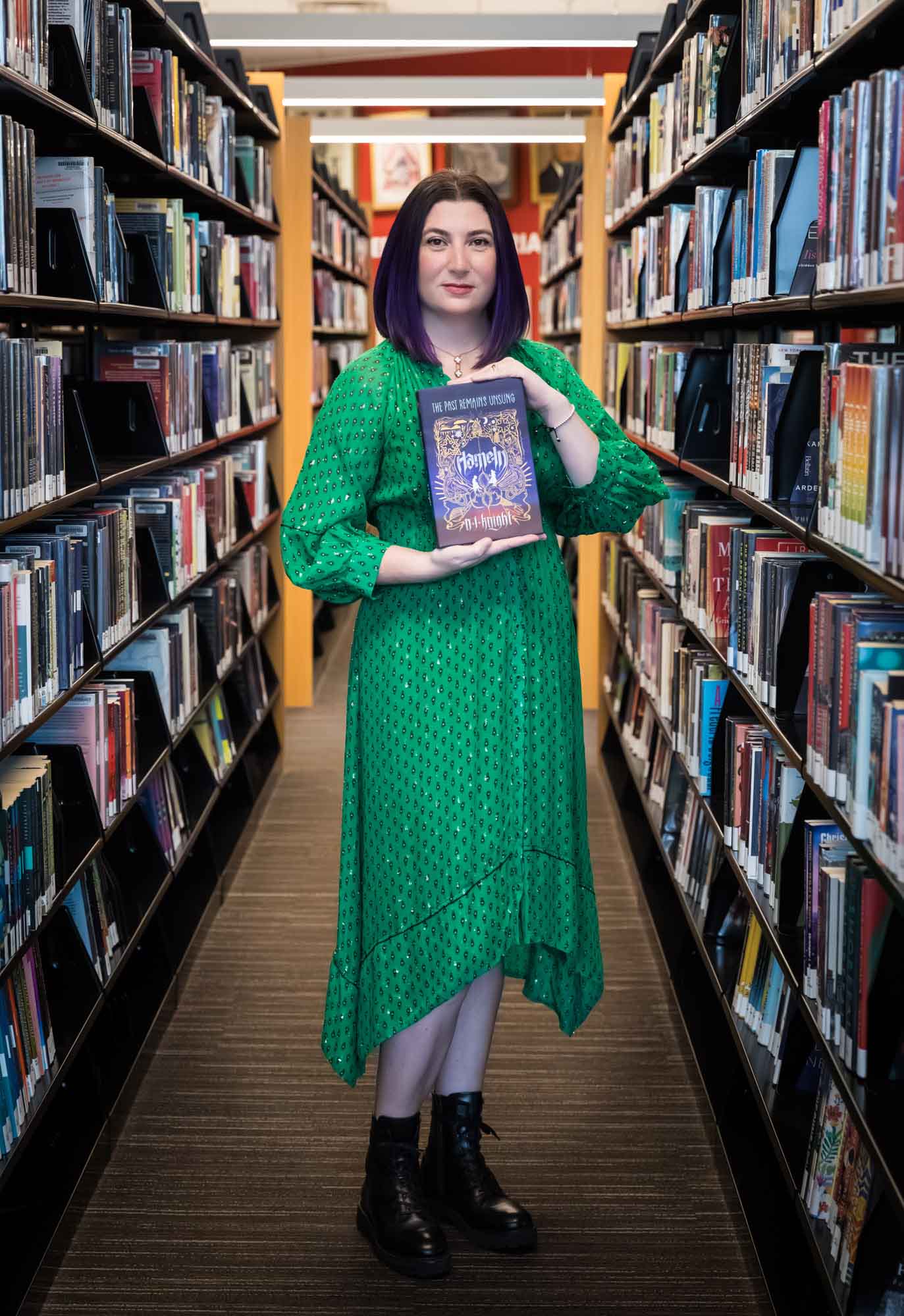 Portrait of author Nancy Knight in the Austin Central Library wearing a green dress holding her book, Hameln