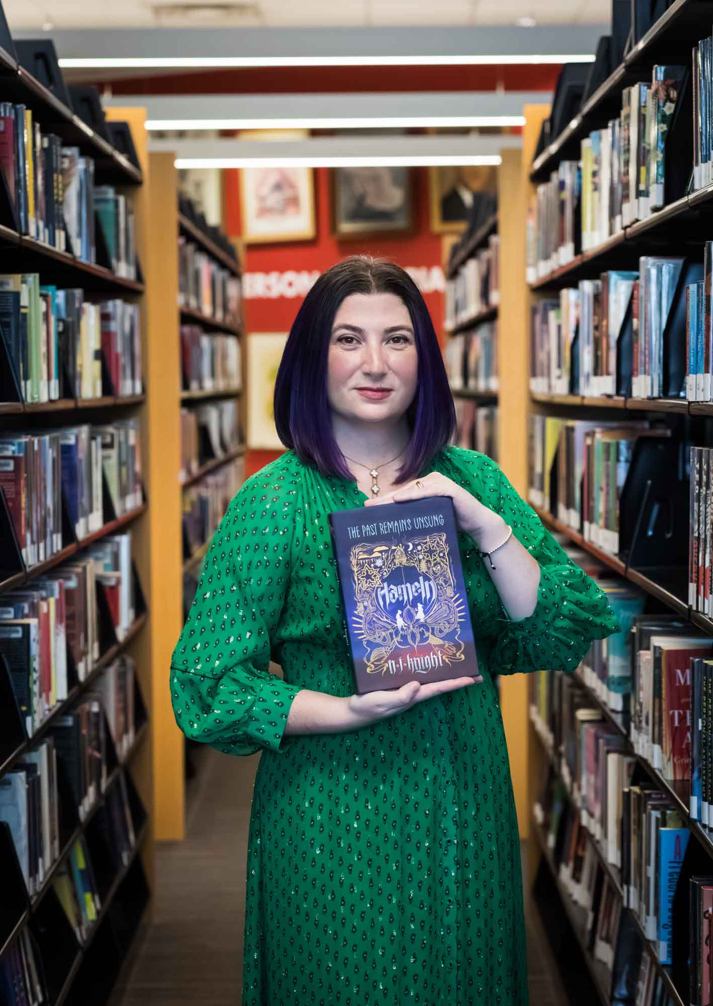 Portrait of author Nancy Knight in the Austin Central Library wearing a green dress holding her book, Hameln