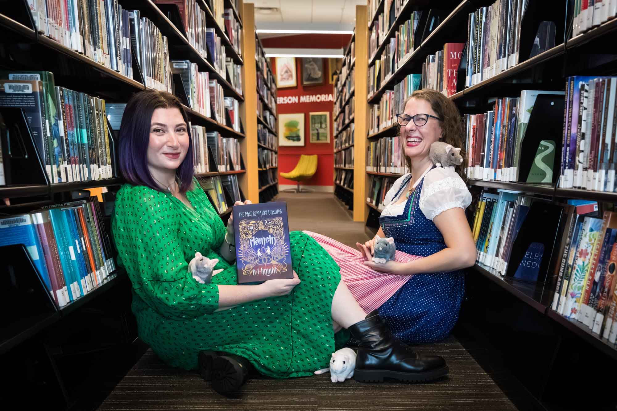 Author Nancy Knight and editor Britta Jensen reading books in front of bookshelves with stuffed mice for an article on how to take photos in the Austin Central Library