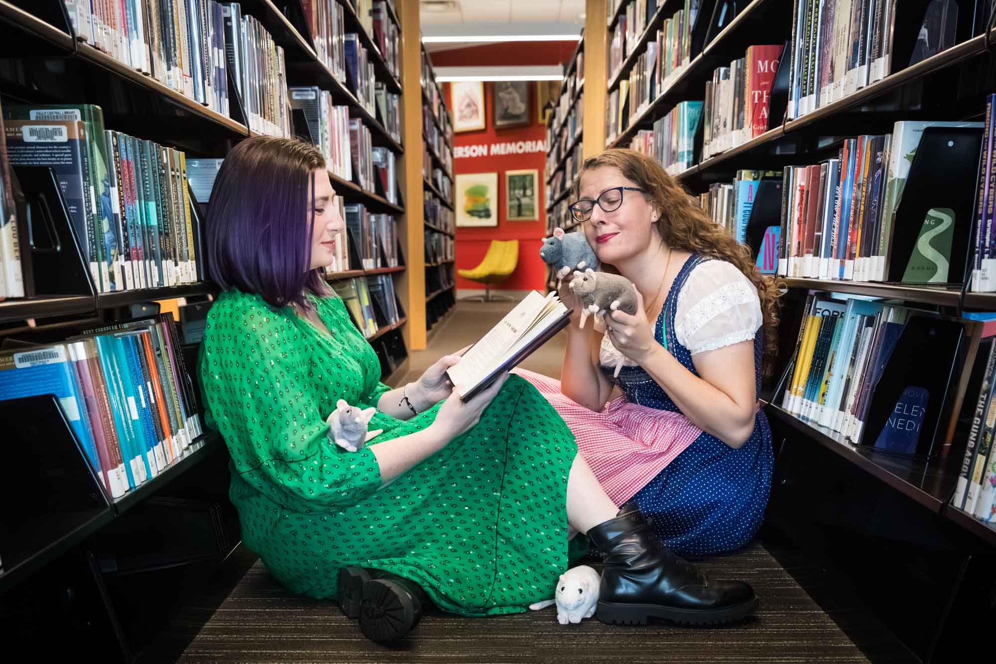 Author Nancy Knight and editor Britta Jensen reading books in front of bookshelves with stuffed mice for an article on how to take photos in the Austin Central Library