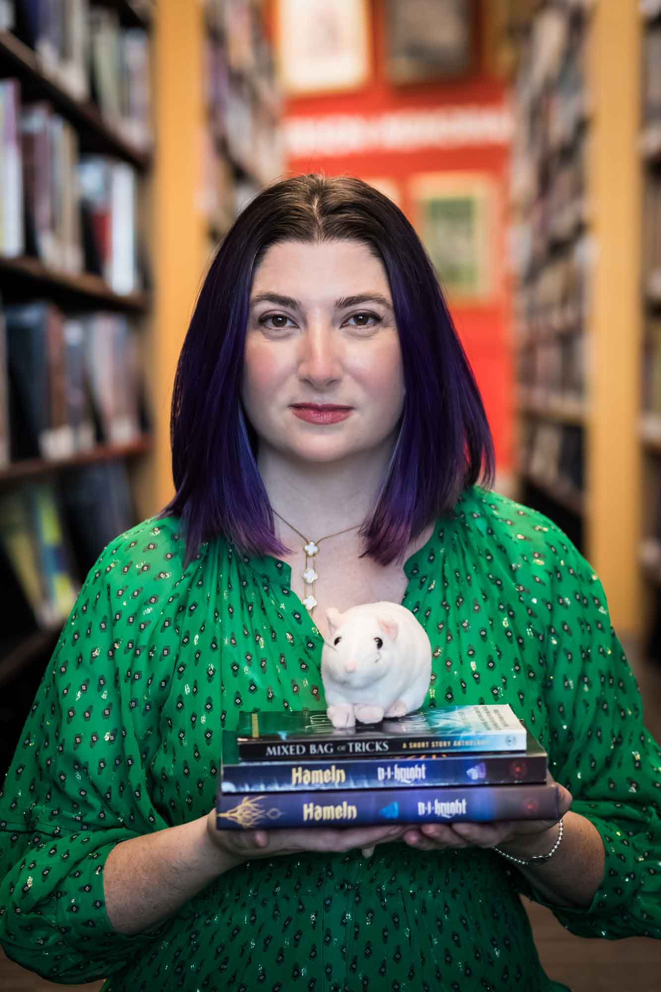 Author Nancy Knight wearing a green dress and holding books and a stuffed mouse for an article on how to take photos in the Austin Central Library
