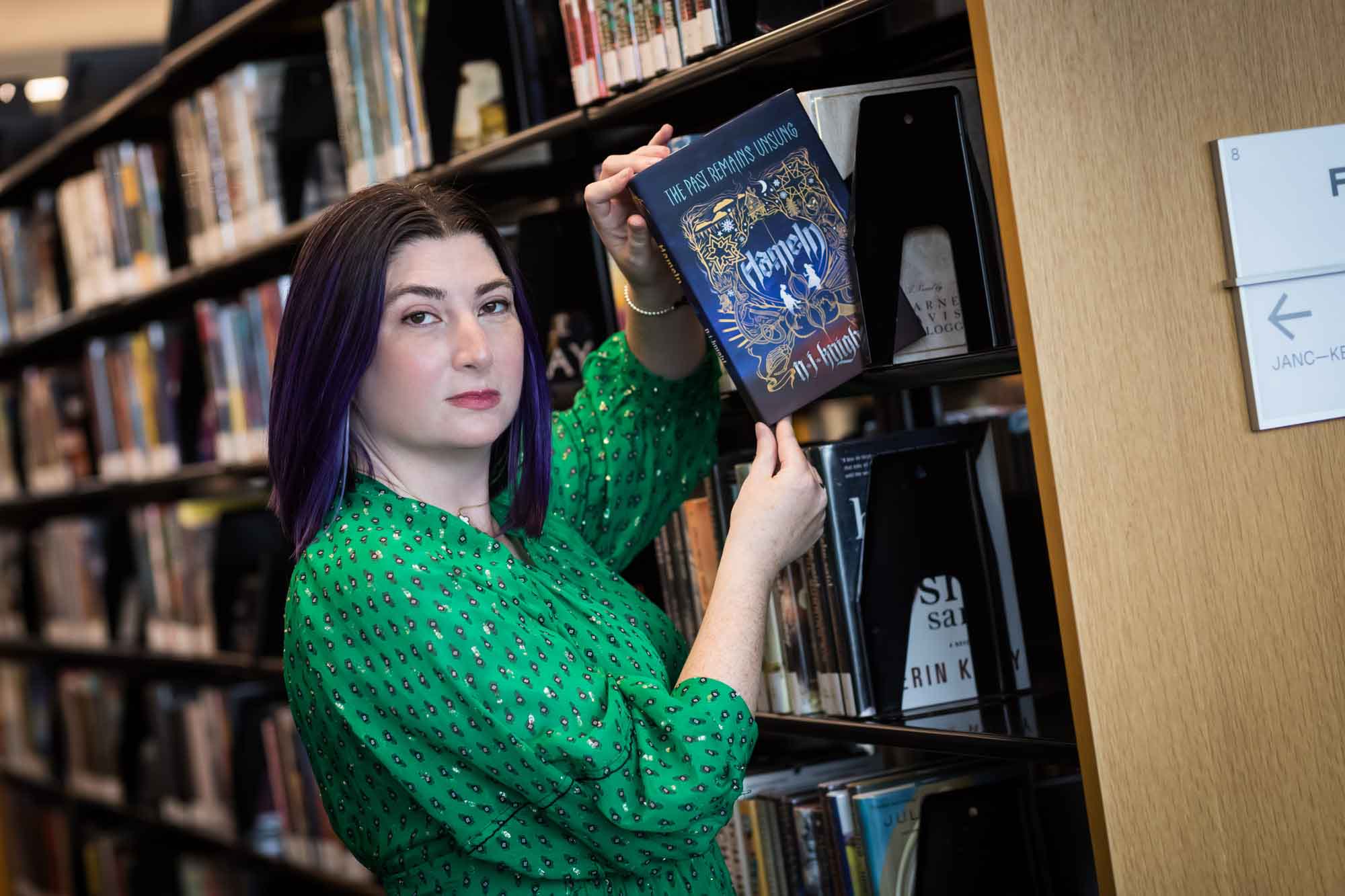 Portrait of author Nancy Knight in the Austin Central Library wearing a green dress holding her book, Hameln
