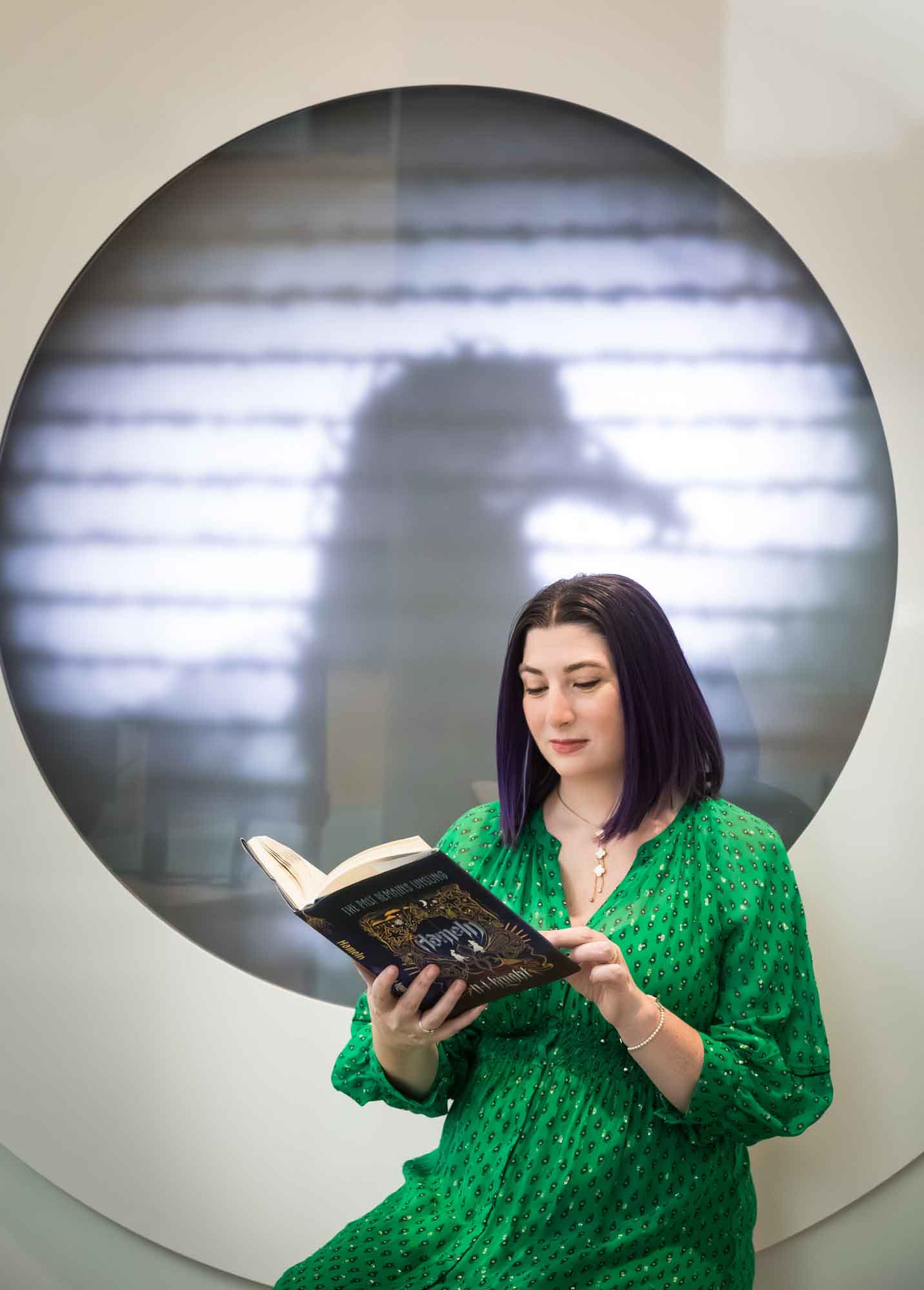 Author portrait of N.J. Knight wearing a green dress and reading her book Hameln in the Austin Central Library in front of a projected raven image