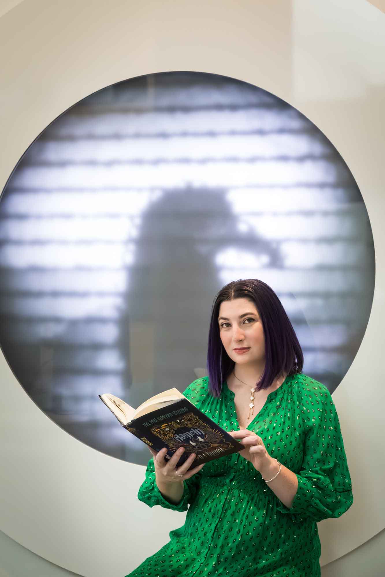 Author portrait of N.J. Knight wearing a green dress and reading her book Hameln in the Austin Central Library in front of a projected raven image