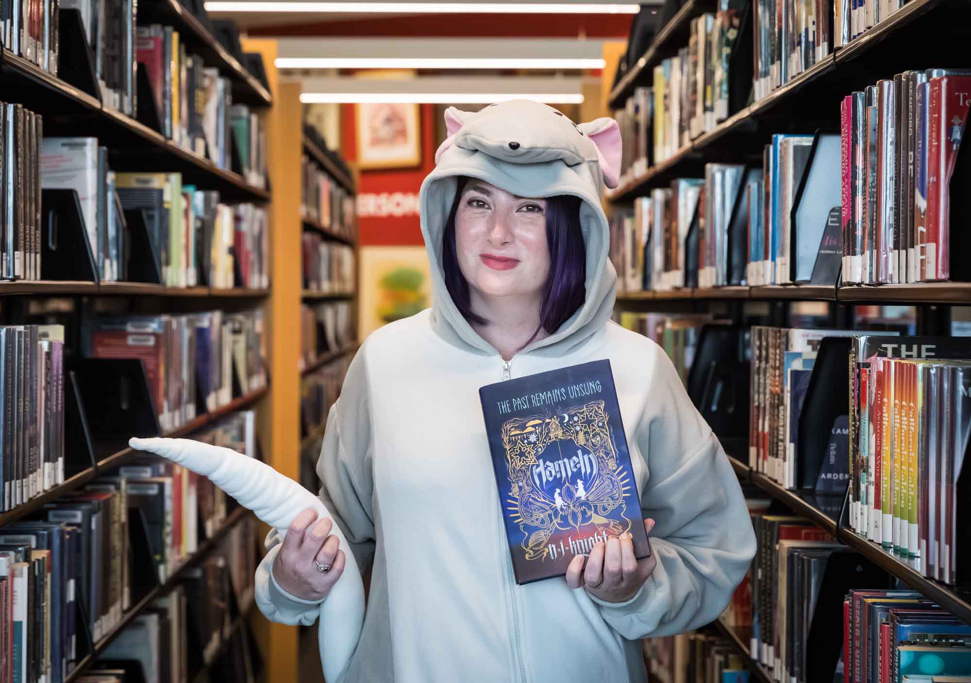 Author Nancy Knight wearing a rat costume and holding her book Hameln for an article on how to take photos in the Austin Central Library