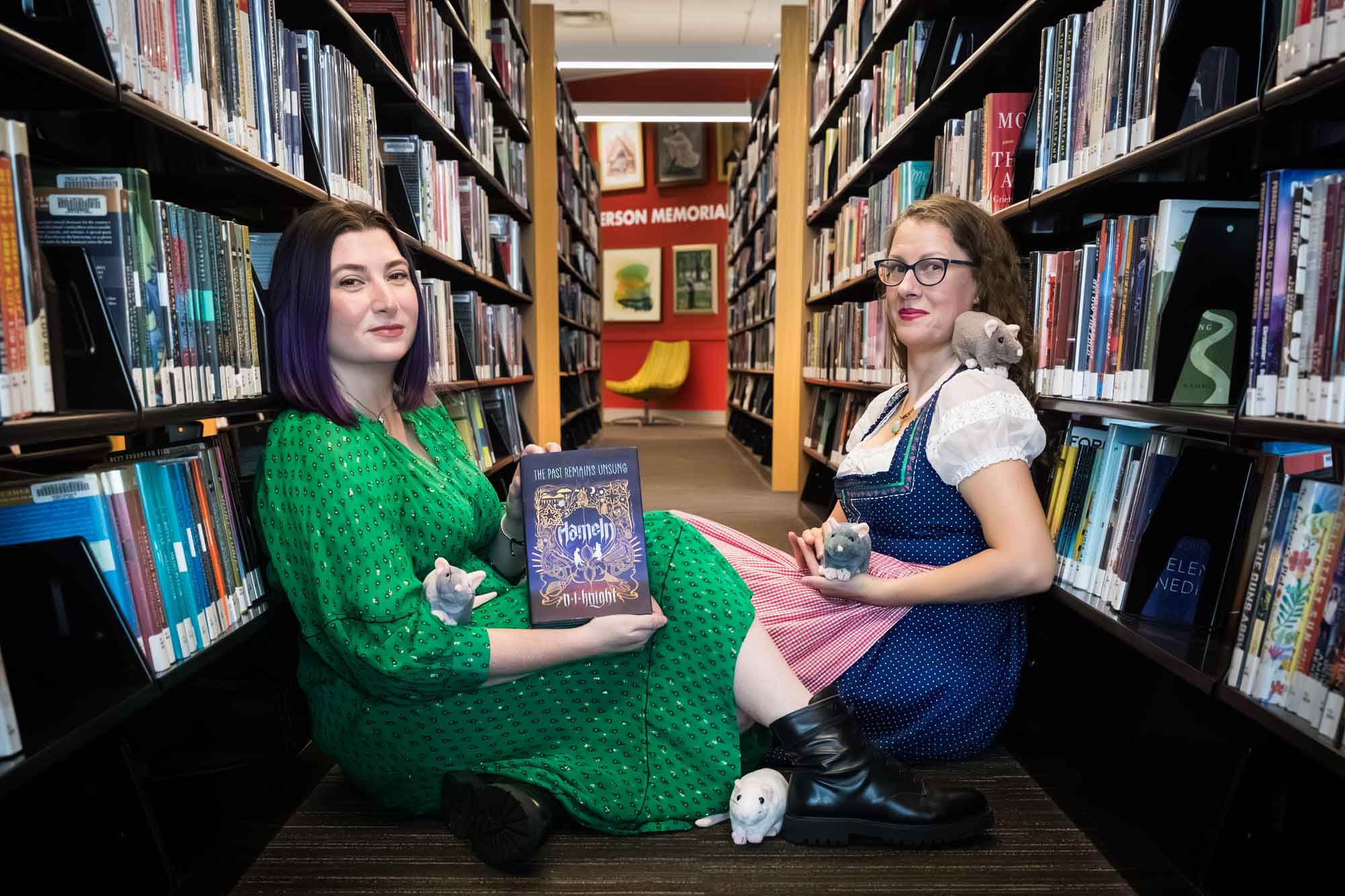 Author Nancy Knight and editor Britta Jensen reading books in front of bookshelves with stuffed mice for an article on how to take photos in the Austin Central Library