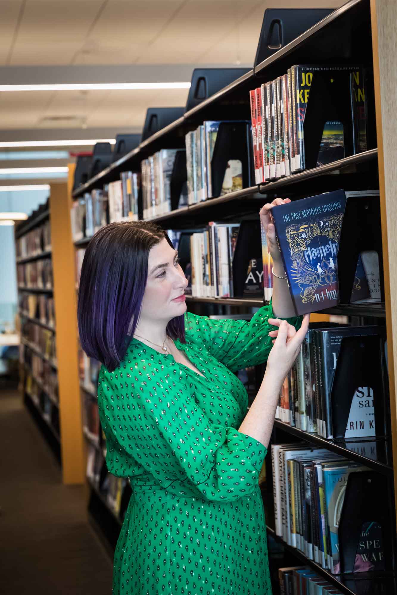 Portrait of author Nancy Knight in the Austin Central Library wearing a green dress holding her book, Hameln