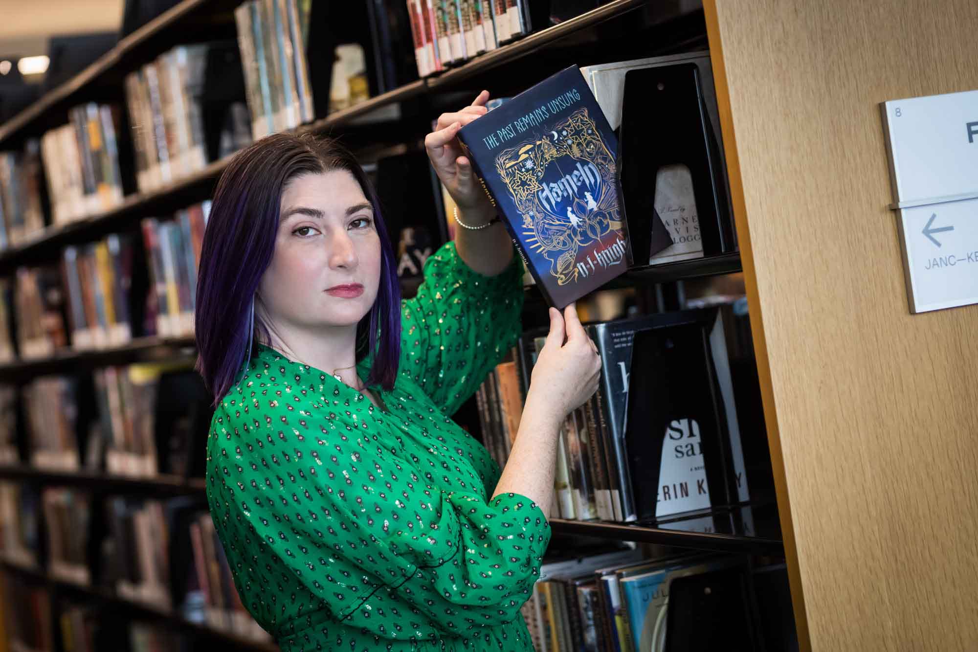 Portrait of author Nancy Knight in the Austin Central Library wearing a green dress holding her book, Hameln