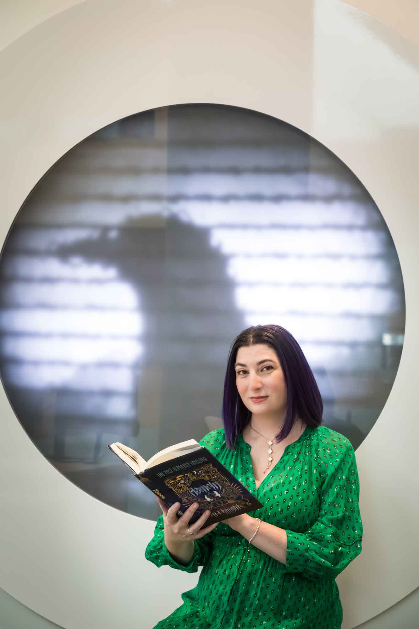 Author portrait of N.J. Knight wearing a green dress and reading her book Hameln in the Austin Central Library in front of a projected raven image