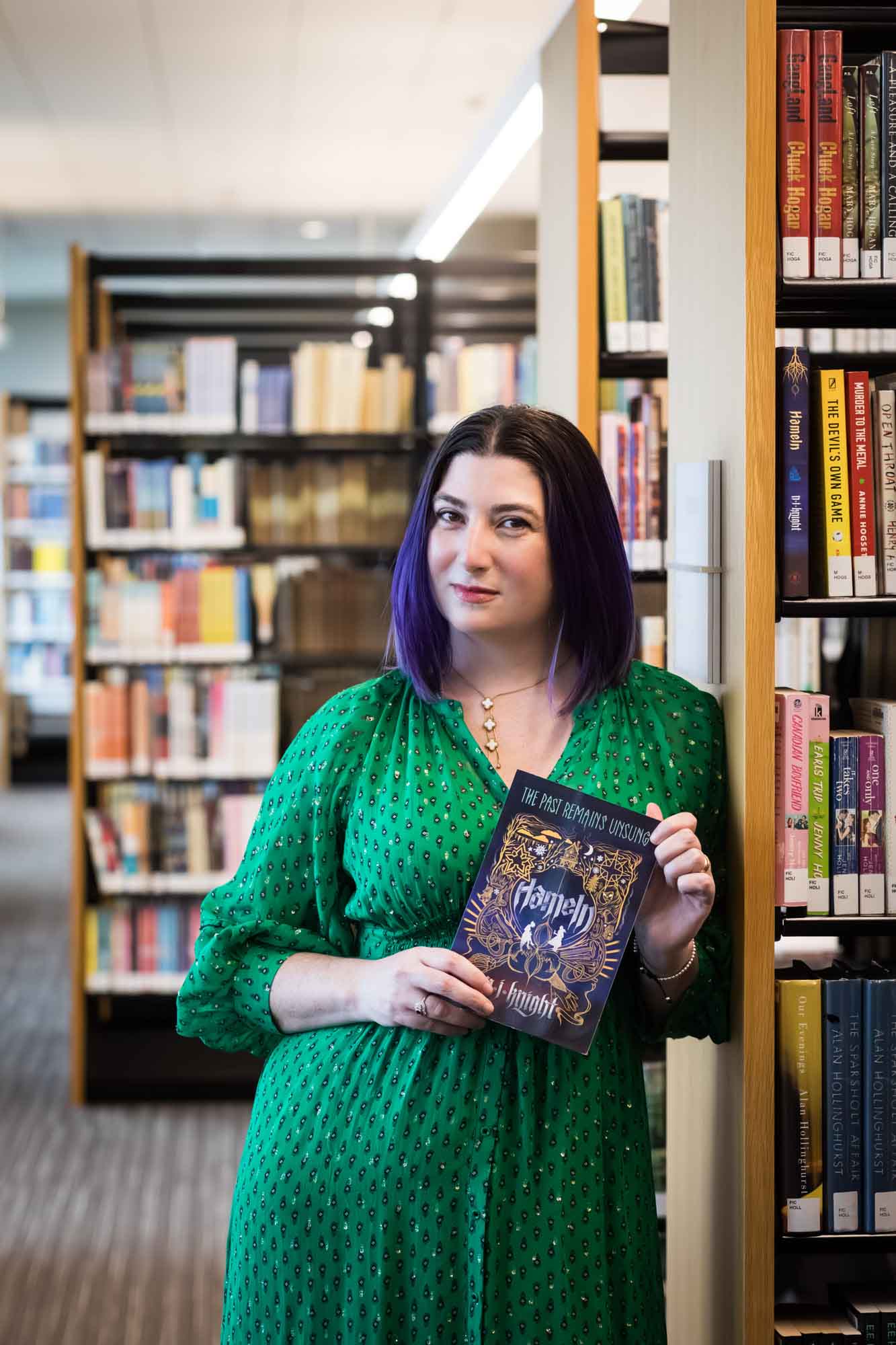 Portrait of author Nancy Knight in the Austin Central Library wearing a green dress holding her book, Hameln