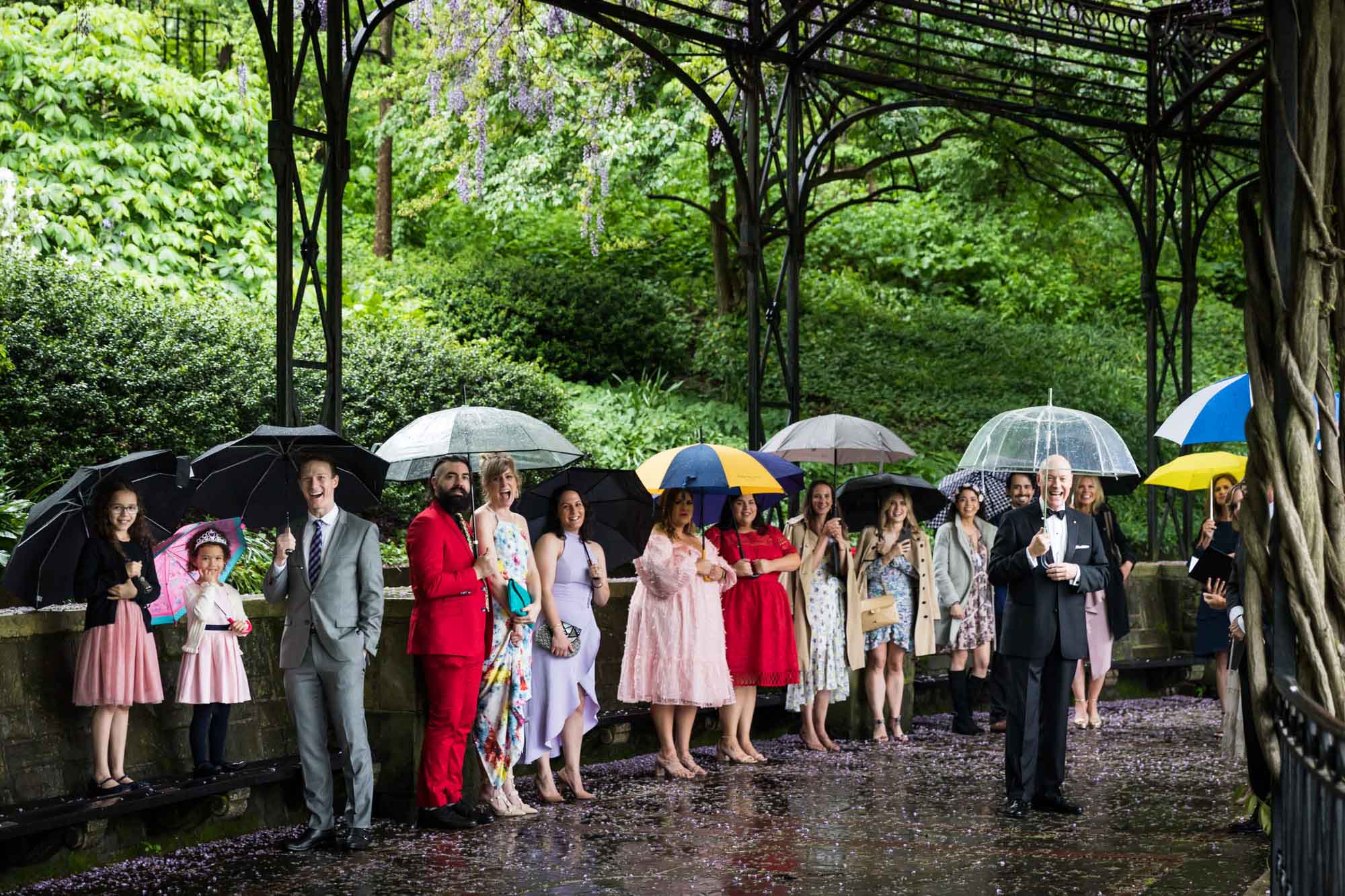 Guests wearing colorful clothes holding umbrellas under Conservatory Garden arch for an article on outdoor wedding tips
