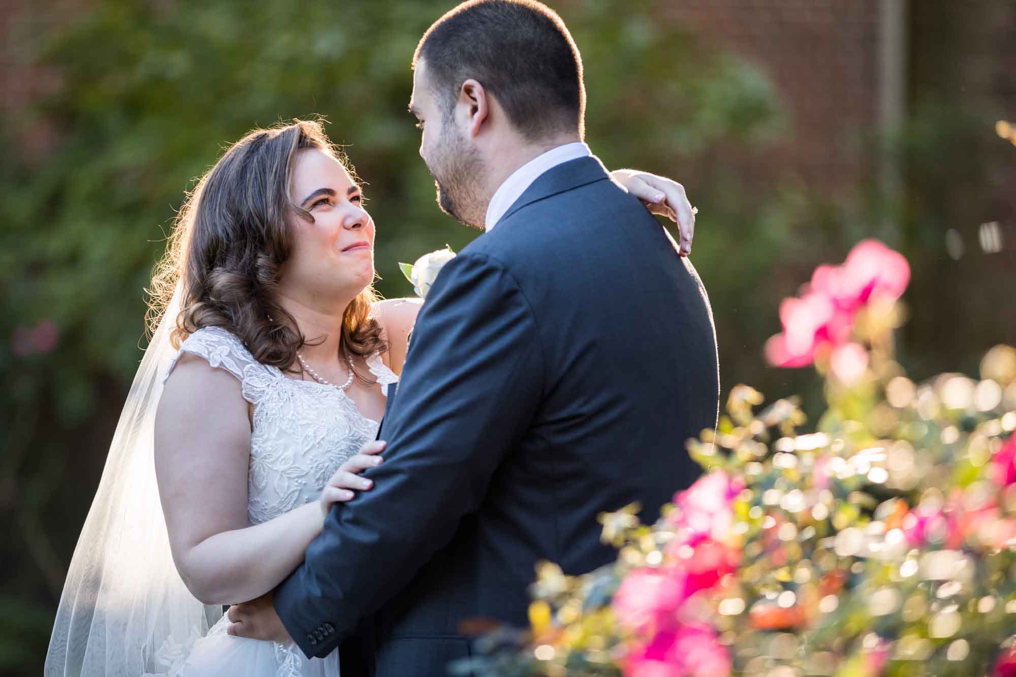 Bride and groom hugging behind rose bush in garden for an article on outdoor wedding tips