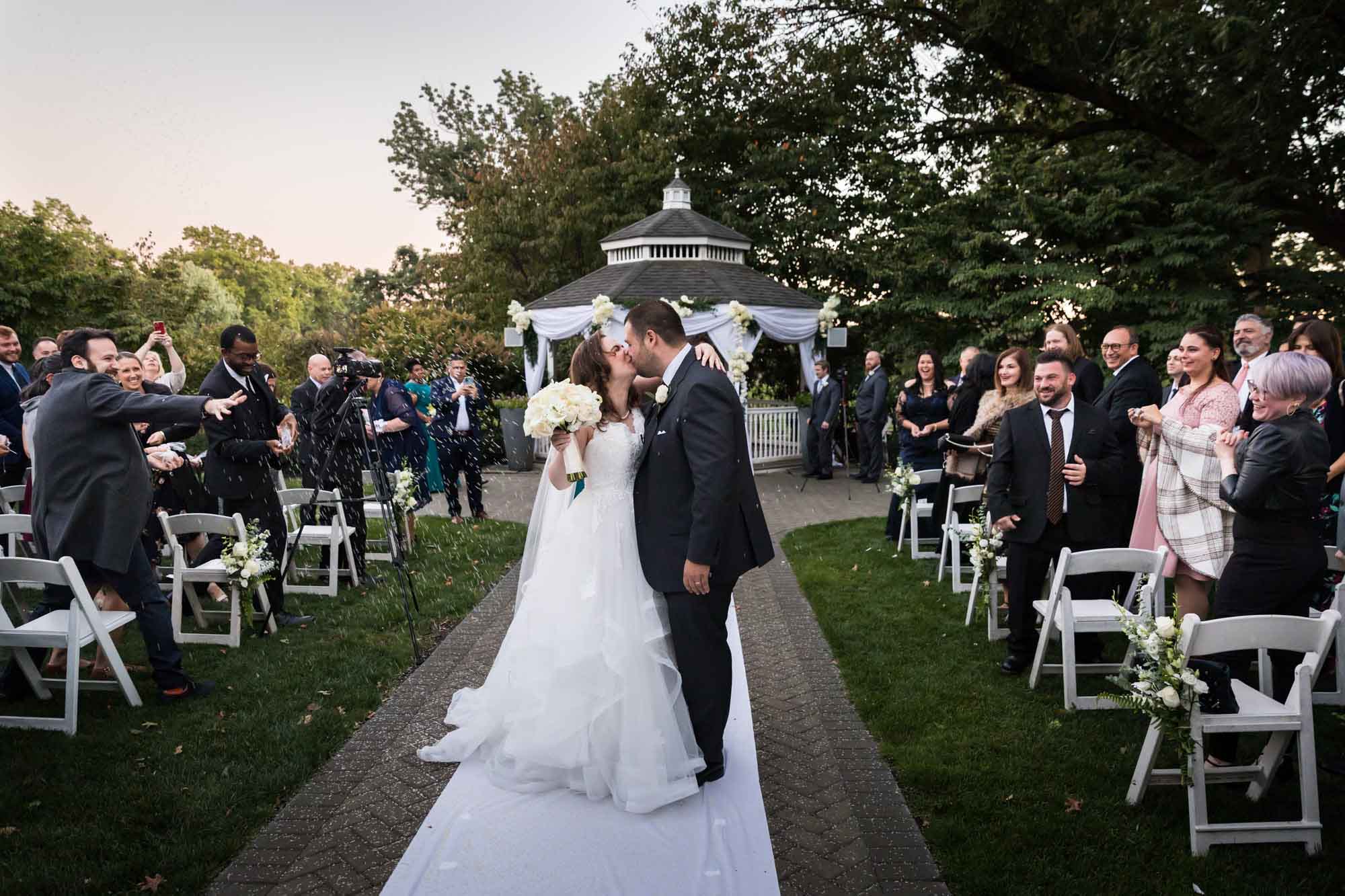 Bride and groom kissing in middle of aisle in front of wedding guests for an article on outdoor wedding tips