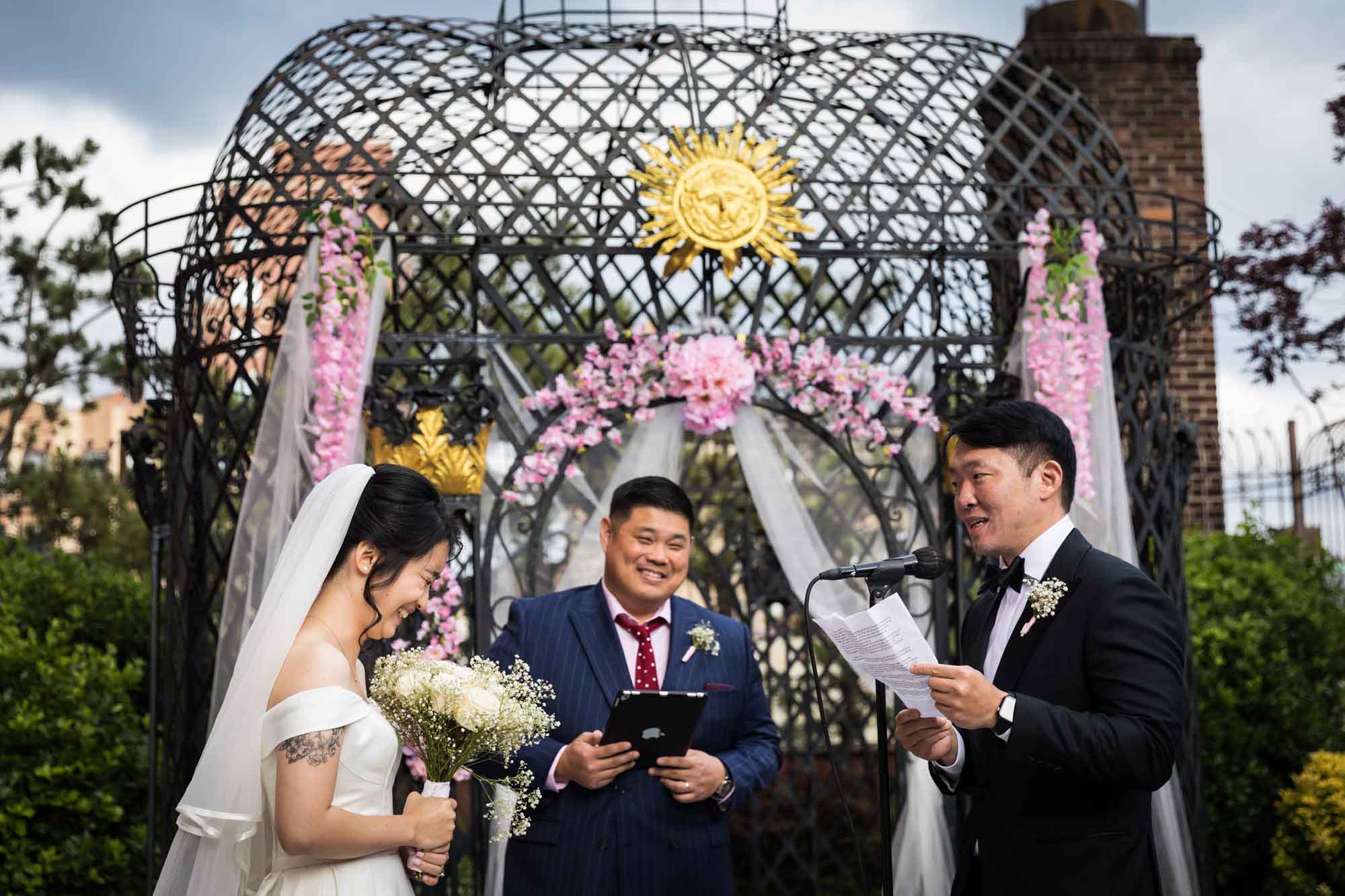 Bride and groom saying vows in front of officiant in front of black iron gazebo for an article on outdoor wedding tips