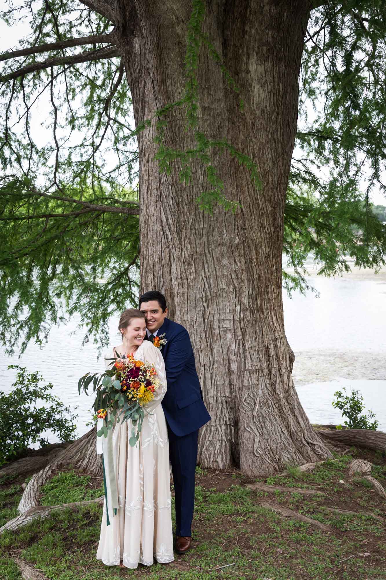 Bride holding colorful flower bouquet with broom beside large tree in Landa Park for an article on outdoor wedding tips