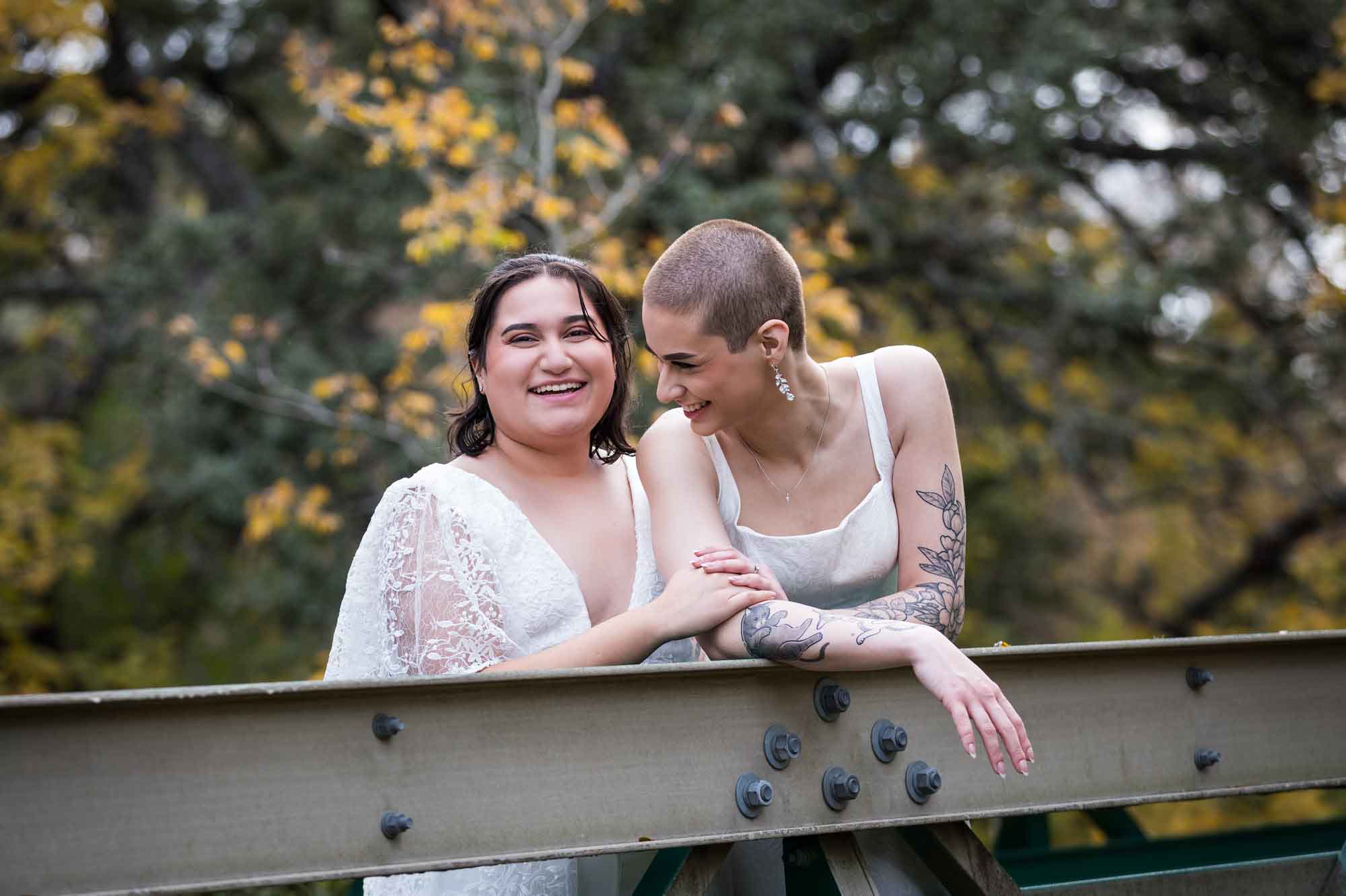 Two brides laughing while leaning against bridge railing for an article on outdoor wedding tips