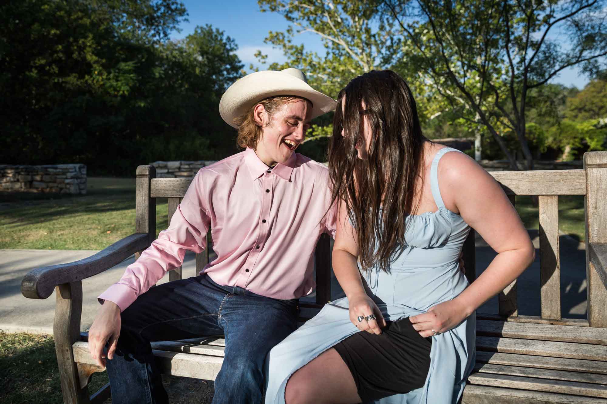 Man wearing pink shirt and cowboy hat and woman wearing blue dress exchanging engagement ring during a San Antonio Botanical Garden engagement shoot