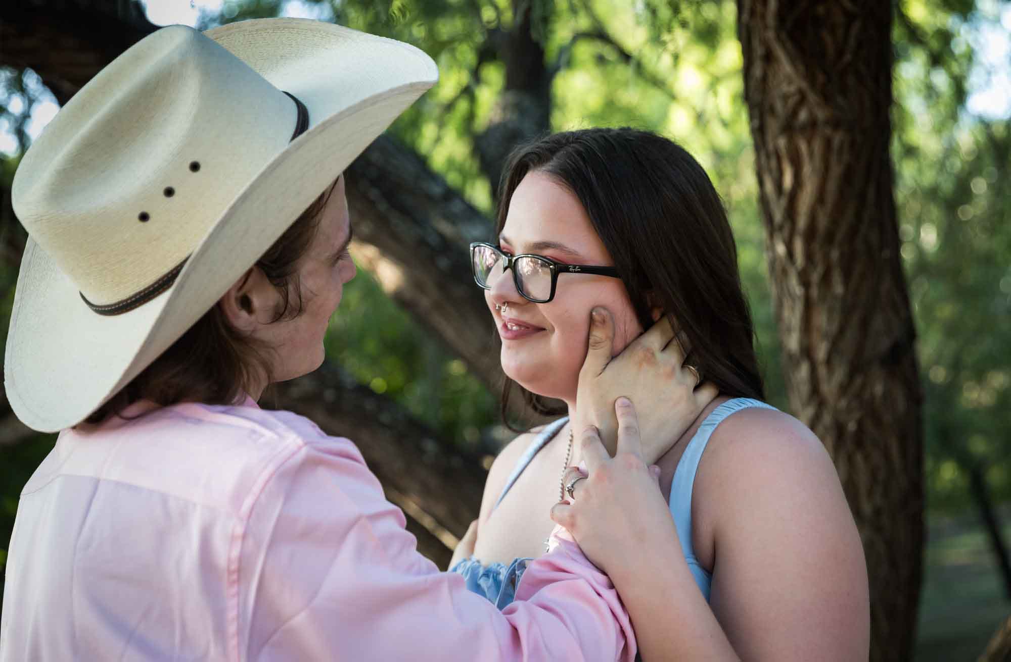 San Antonio Botanical Garden engagement photos of man wearing pink shirt and cowboy hat with hand on woman's face
